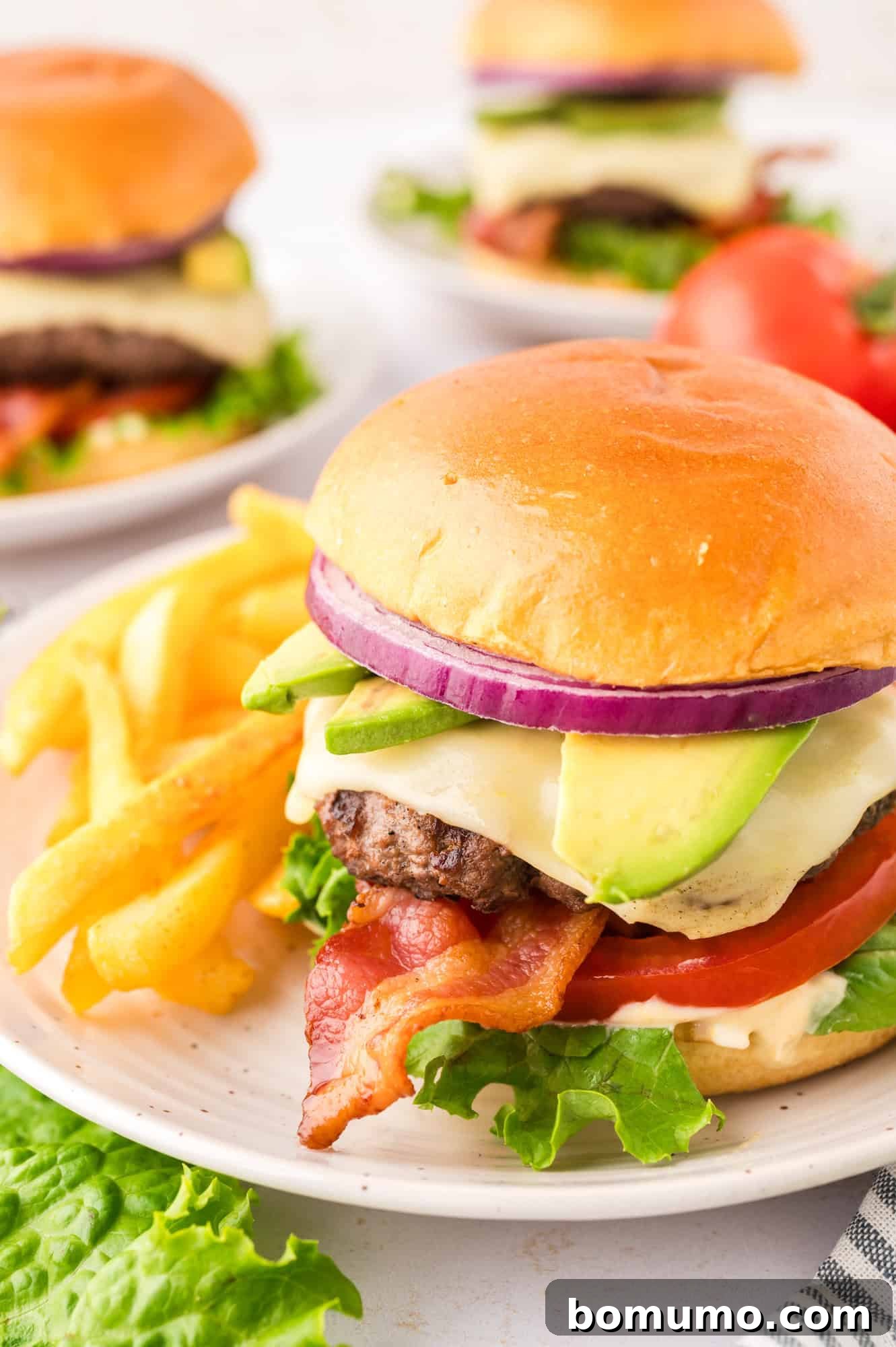 The Cali Dream Burger 18 A perfectly plated California burger on a brioche bun, featuring a juicy beef patty, crispy bacon, fresh lettuce, tomato, onion, avocado, and a generous dollop of sauce.