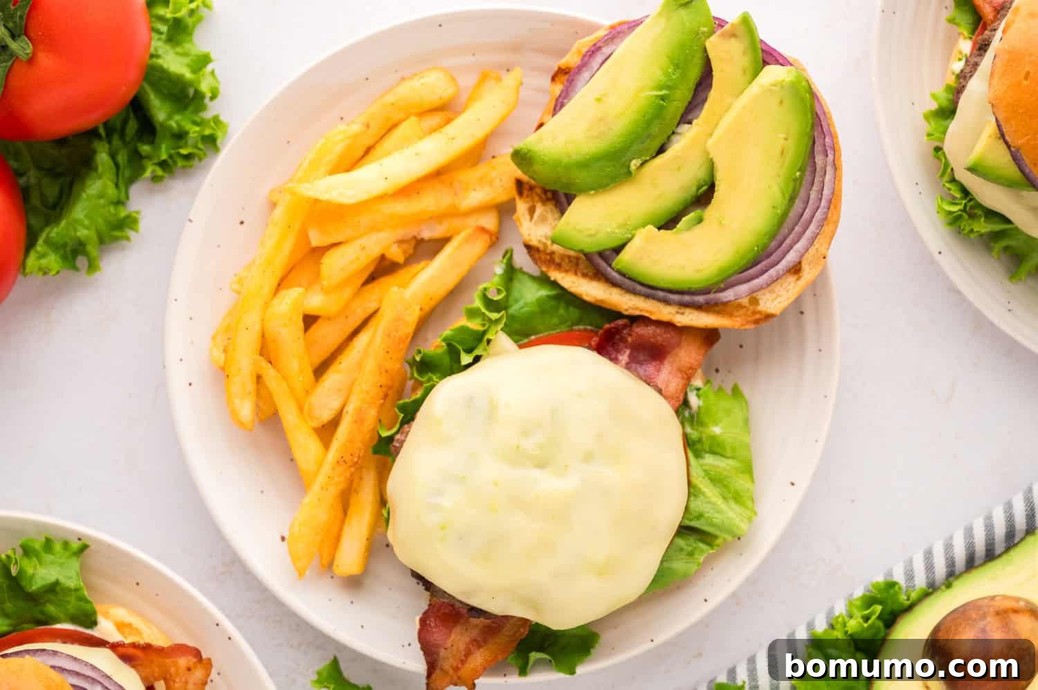 The Cali Dream Burger 3 An open-faced California burger, revealing layers of melted cheese, bacon, avocado, and fresh vegetables on a toasted bun.