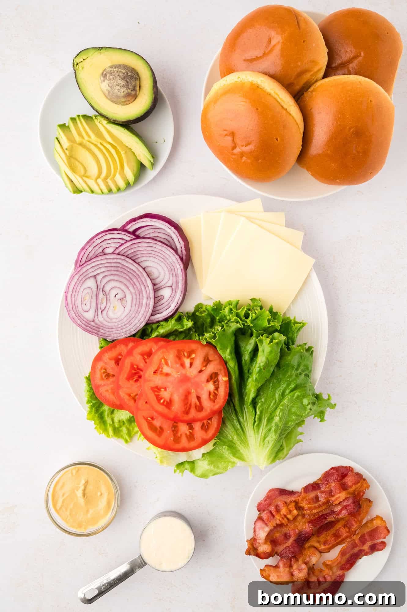 The Cali Dream Burger 5 Various fresh toppings and condiments for burgers, including sliced avocado, tomatoes, lettuce, and the creamy sauce, ready for assembly.