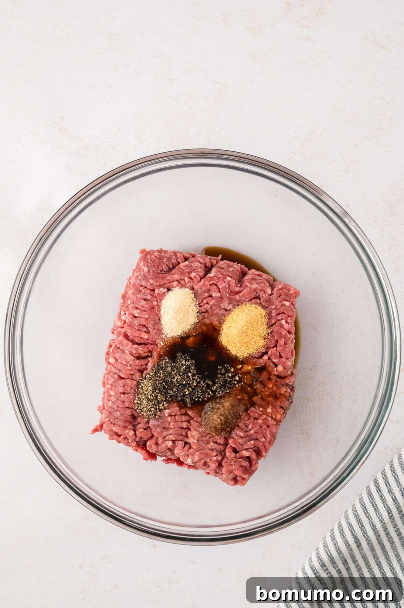The Cali Dream Burger 6 Ground beef with a generous sprinkling of seasonings on top, ready to be mixed.