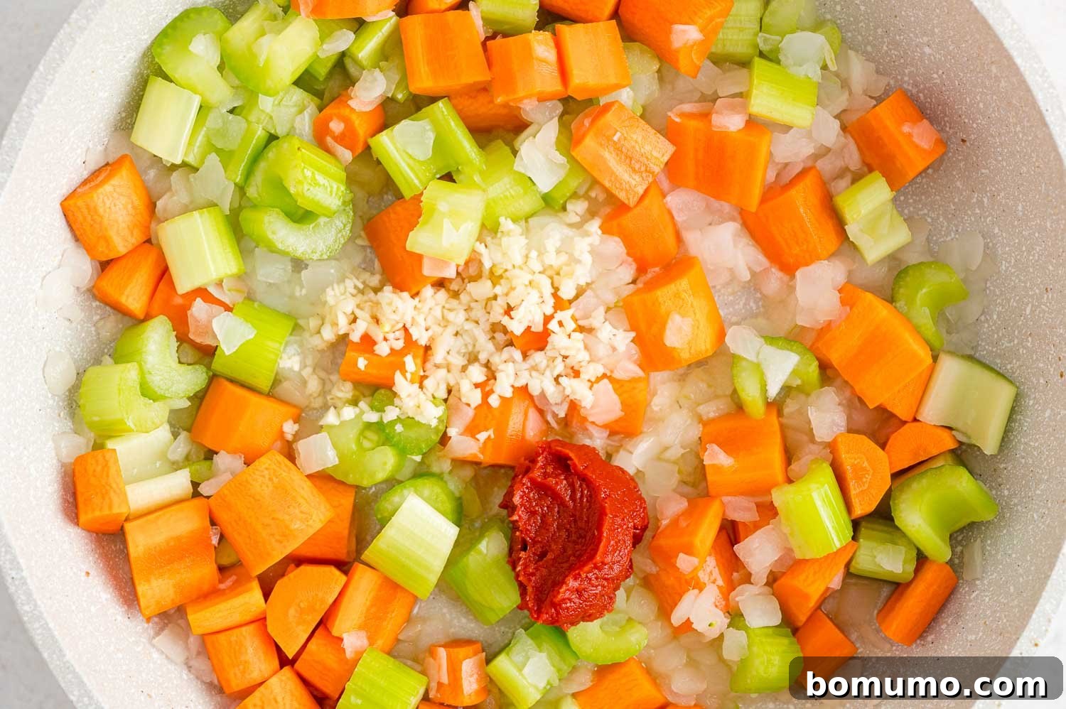Tomato paste and minced garlic added to the sautéed vegetables in a pan, enhancing the stew's rich flavor base.