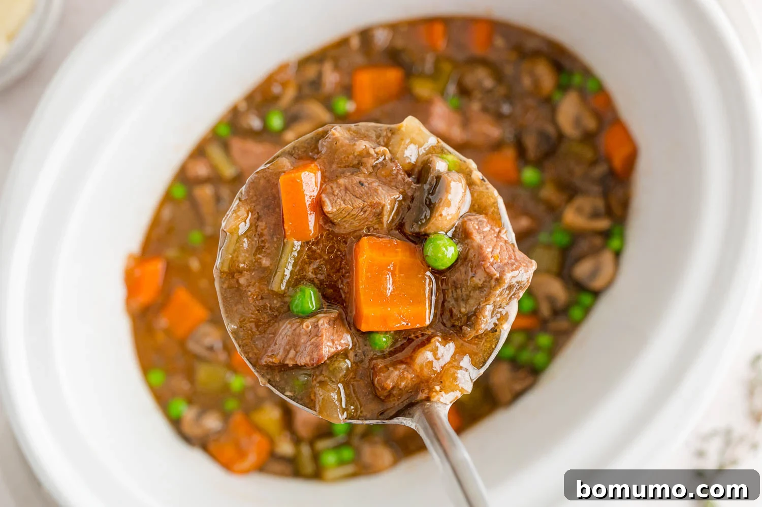 A generous scoop of rich beef Marsala stew being lifted from the crockpot with a ladle, showcasing its thick, savory gravy and tender ingredients.