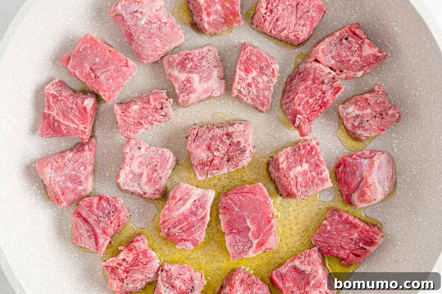 Unbrowned beef cubes coated in flour, salt, and pepper, ready for searing in a hot pan.