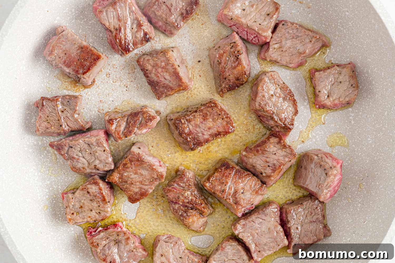 Perfectly browned beef cubes sizzling in a pan, developing a rich, caramelized crust before being added to the slow cooker.