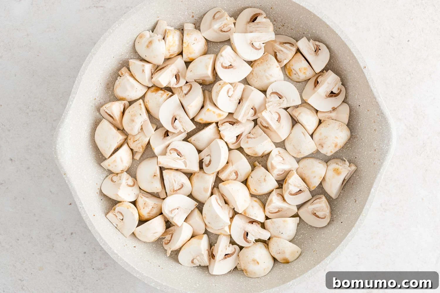 Raw mushroom quarters laid out in a hot skillet, ready to be sautéed to perfection.