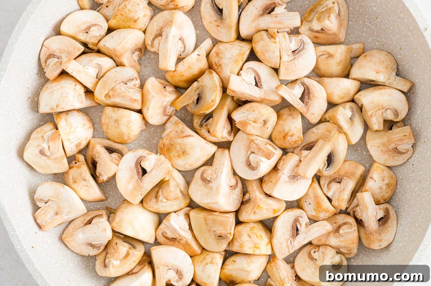 Mushroom quarters, slightly browned and softened, cooking gently in a skillet.