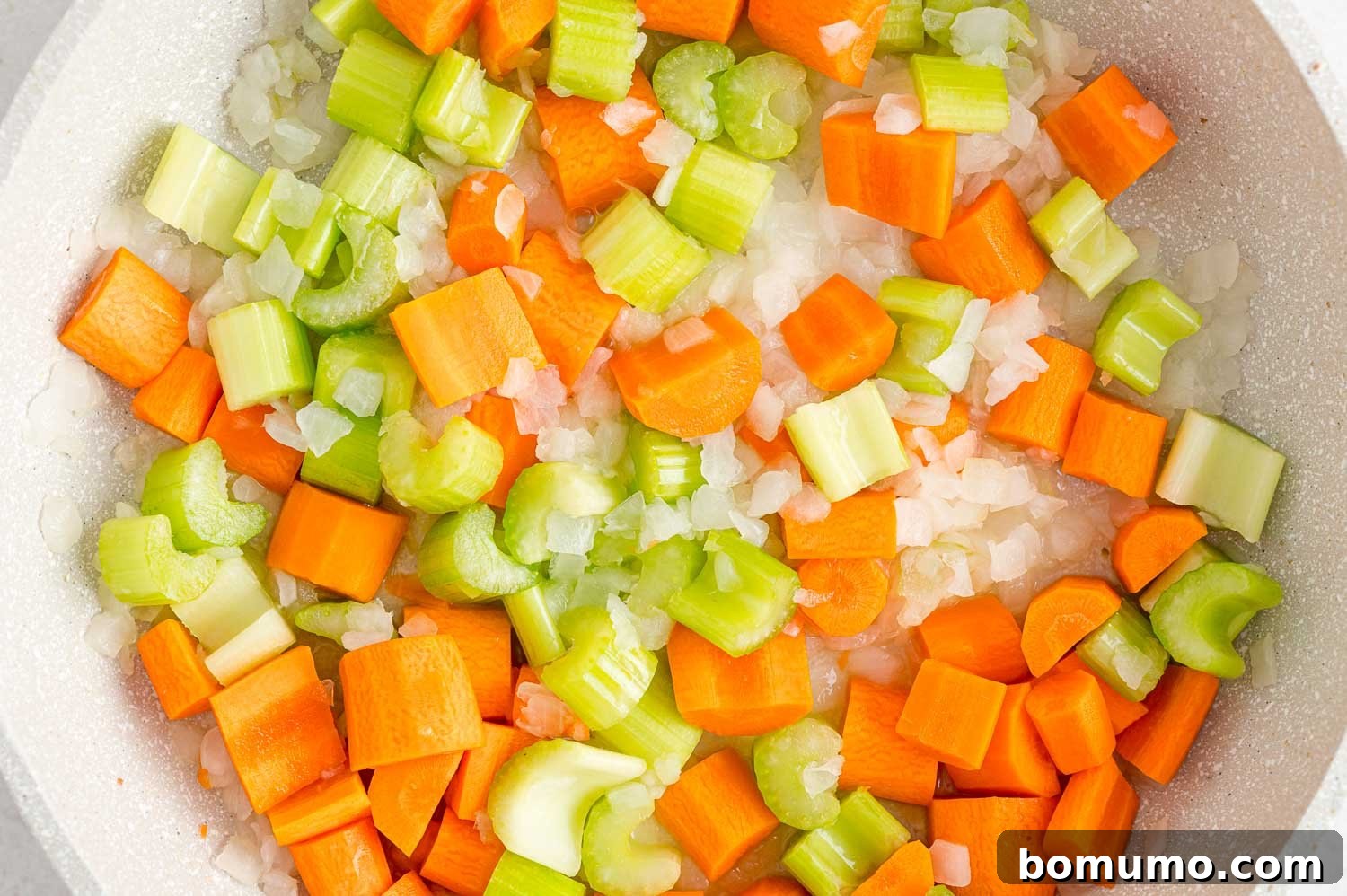 A colorful medley of carrots, celery, and onions being sautéed in a hot pan, softening and releasing their aromas.