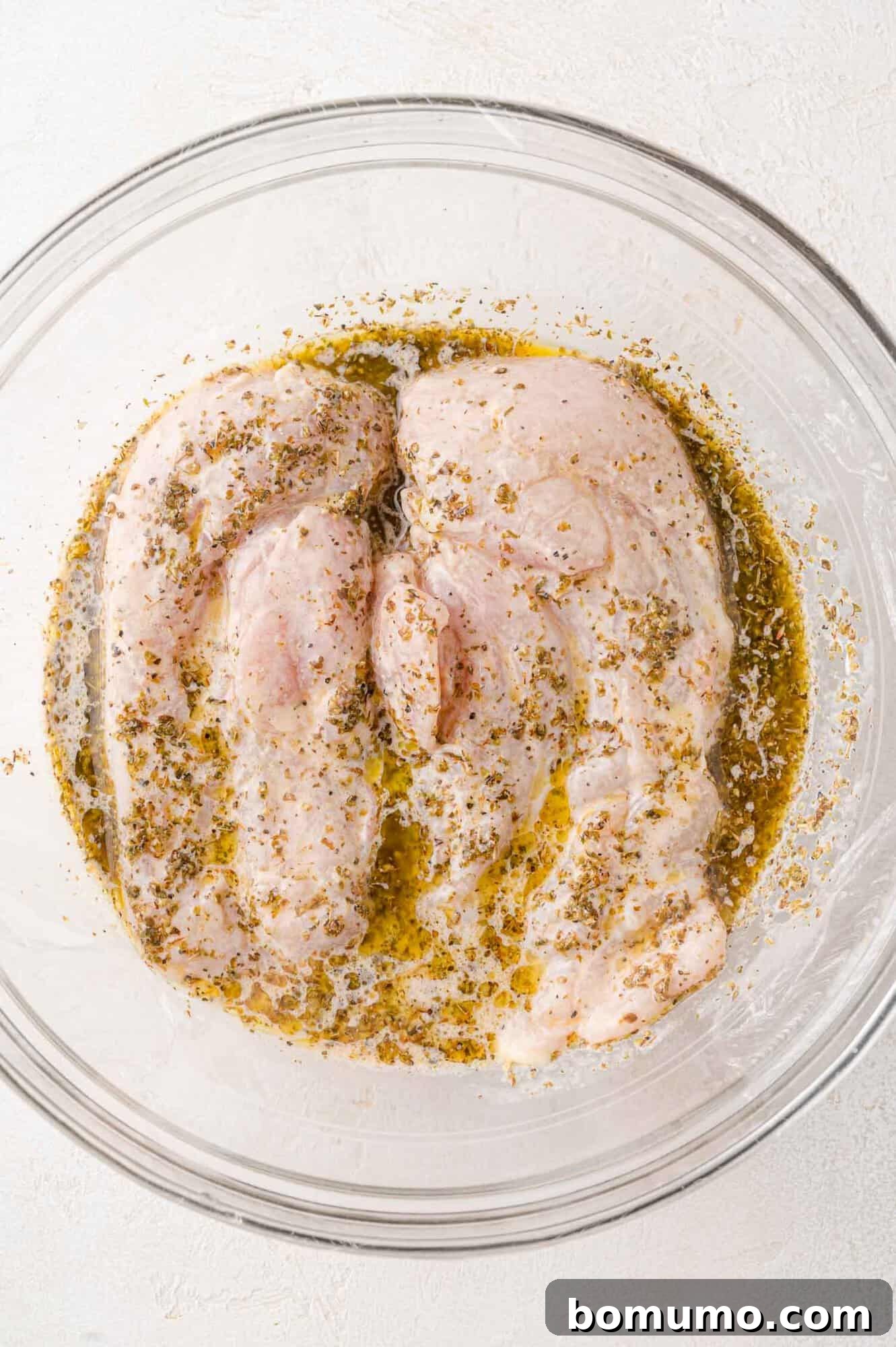 Chicken breasts fully coated in Greek marinade, resting in a bowl.