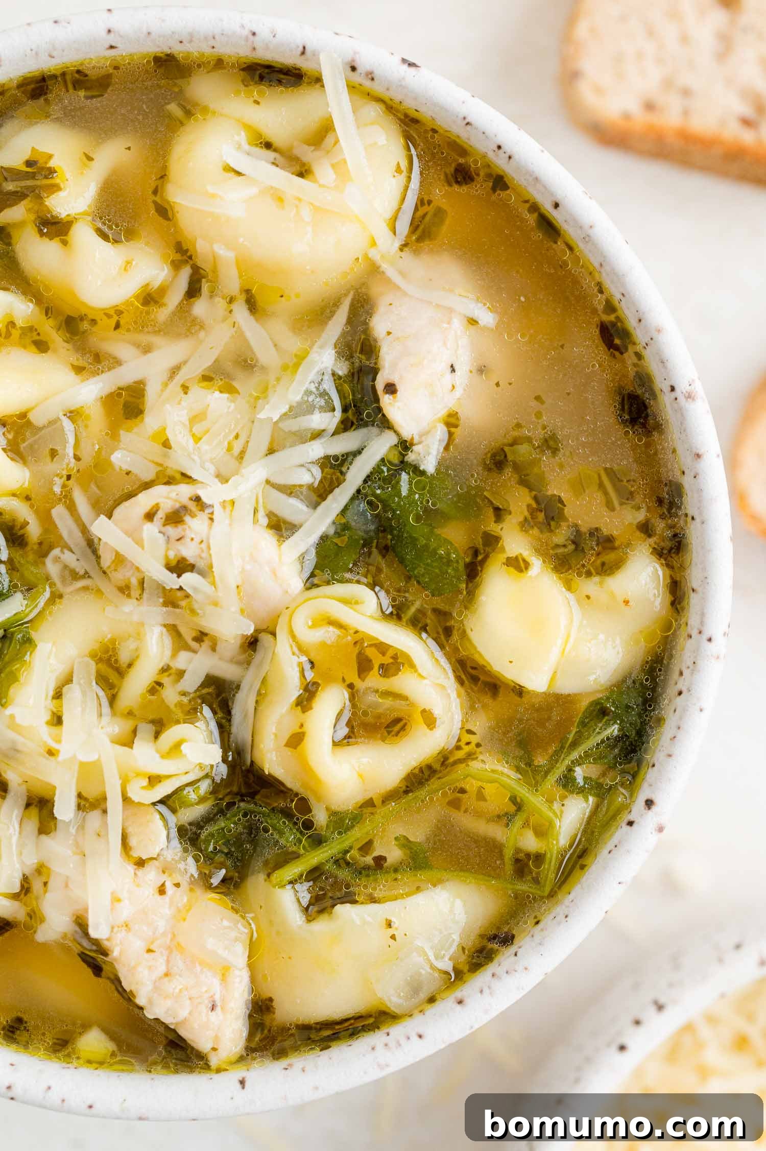 A vibrant bowl of chicken tortellini soup with fresh kale and a swirl of pesto, presented in a white ceramic bowl.