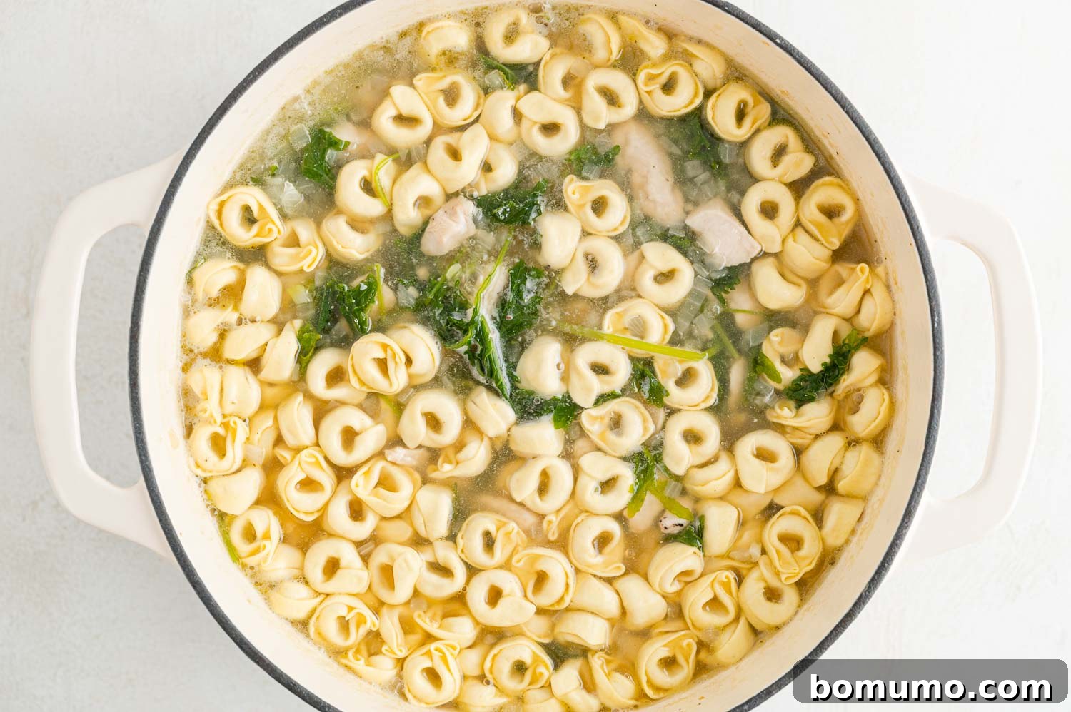 Dried cheese tortellini being carefully added to the simmering soup, ready to cook.