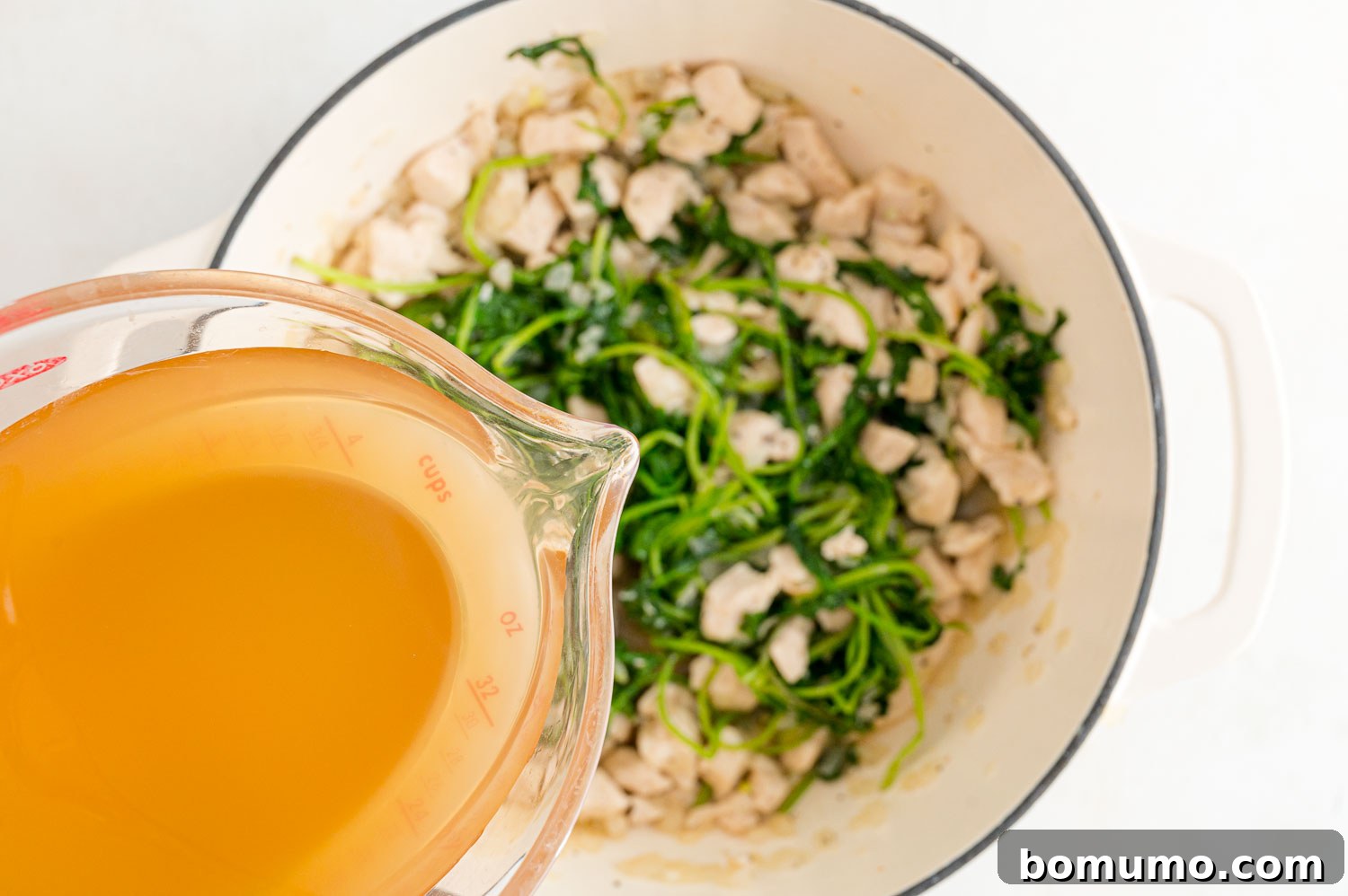 Rich chicken broth being poured into the pot, combining with the cooked chicken, onions, garlic, and kale.
