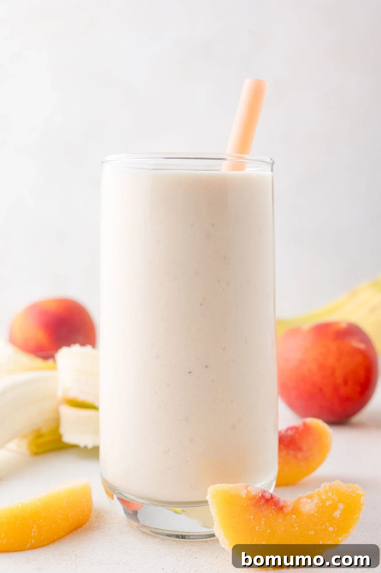 A vibrant, creamy peach banana cottage cheese smoothie served in an elegant glass with a straw, surrounded by fresh peach slices, ripe bananas, and whole peaches against a soft, light backdrop.