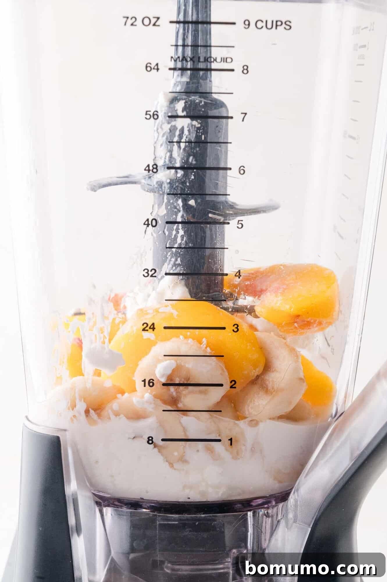 A close-up, side view of a blender pitcher filled with a colorful medley of frozen peach slices, sweet banana chunks, and creamy cottage cheese, illustrating the initial stages of smoothie preparation before blending.