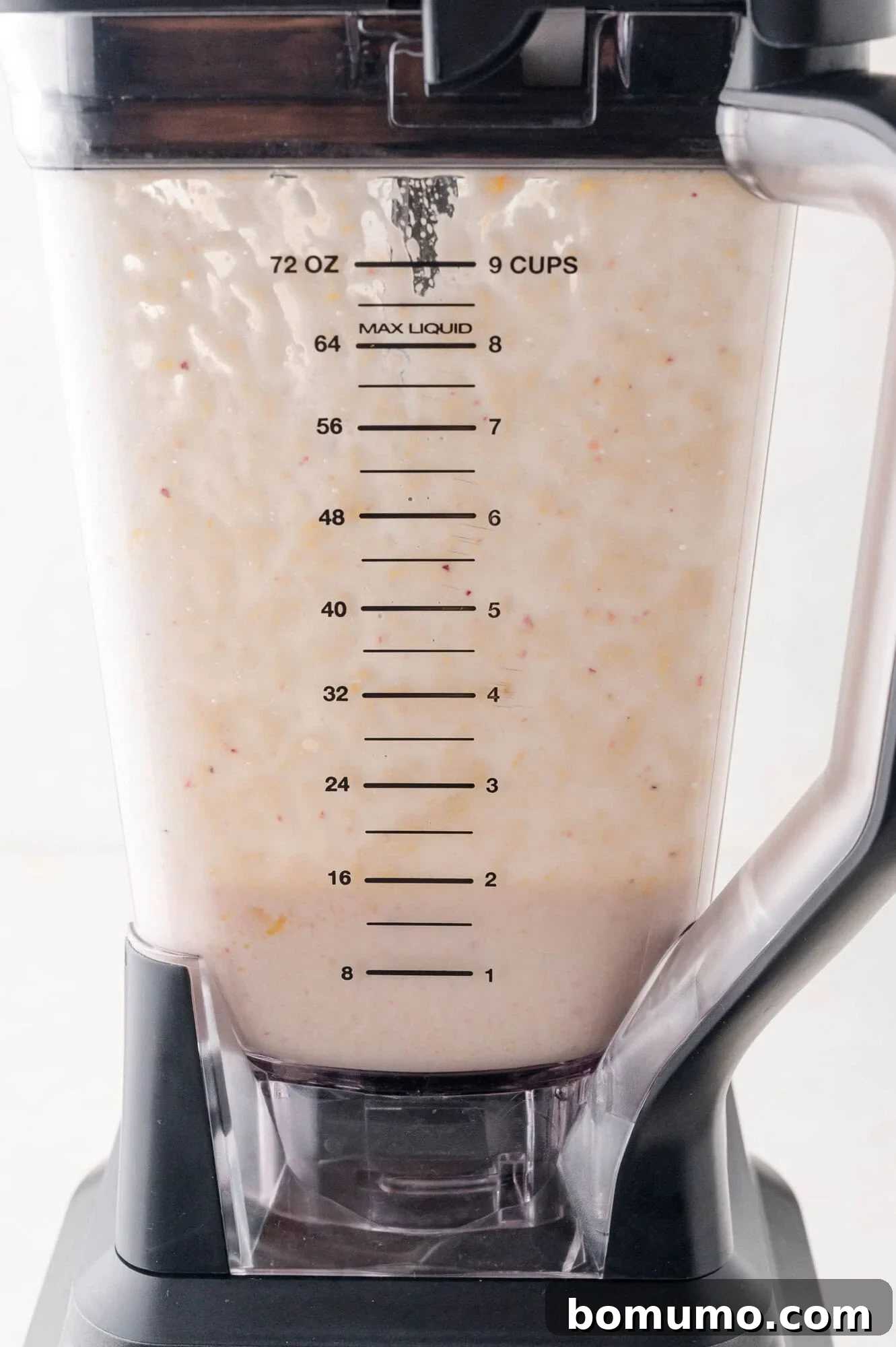A blender pitcher, marked with volume measurements up to 72 ounces or 9 cups, filled with a perfectly smooth, creamy, and light-colored mixture, indicating a thoroughly blended cottage cheese smoothie ready to be served.