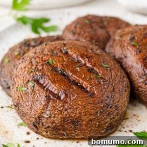 Grilled portobello mushrooms placed on a white plate and garnished with fresh parsley.