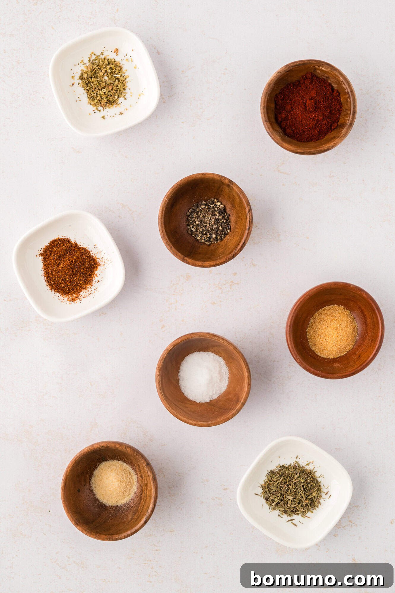 A vibrant collection of individual spices, each in its own small bowl, laid out neatly for a homemade blackening seasoning blend.