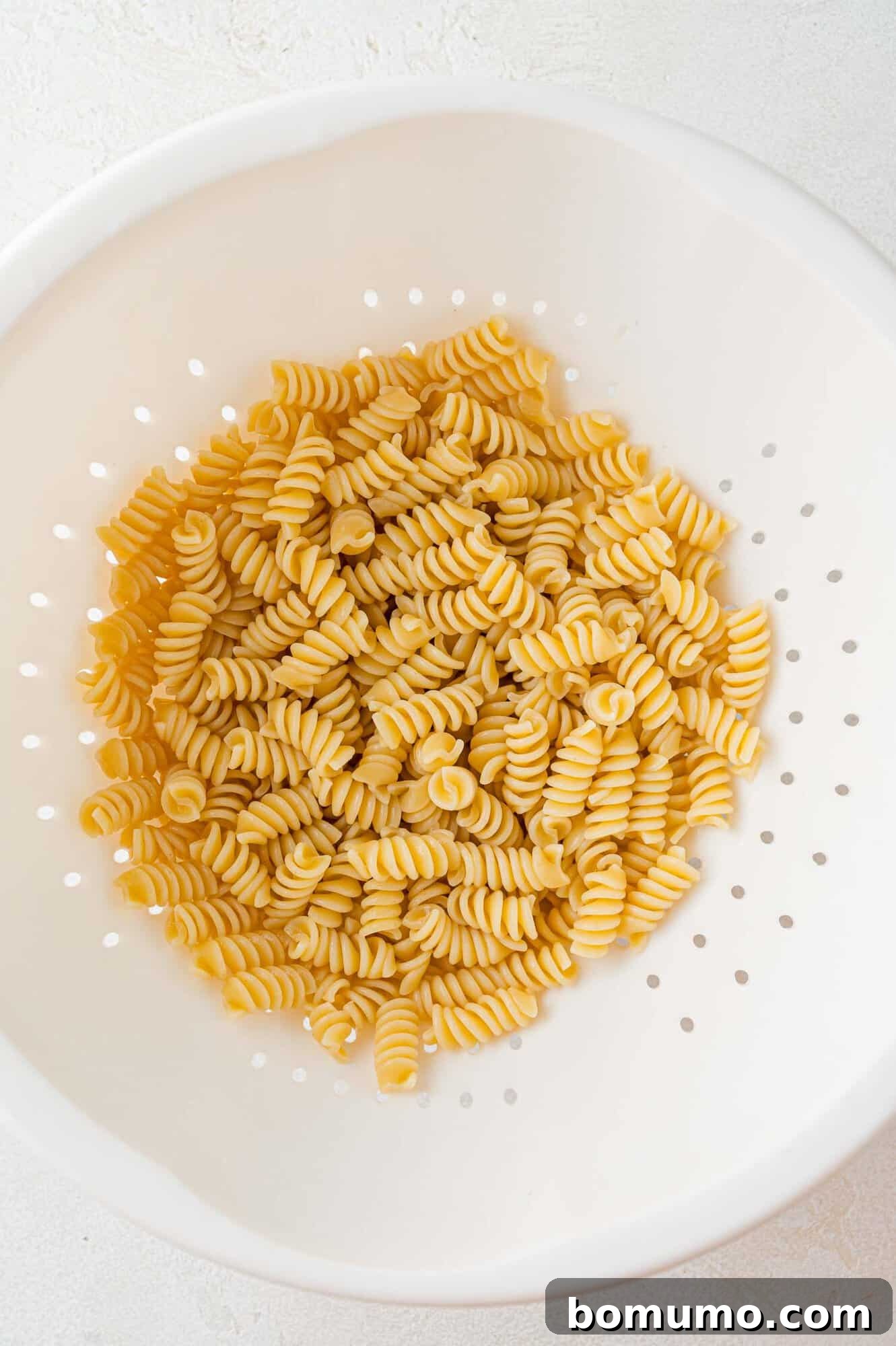 Freshly cooked rotini pasta, perfectly drained and cooled in a colander, ready for the salad assembly.