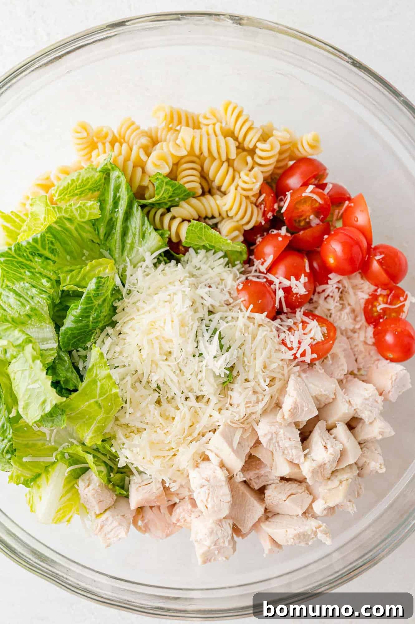All the vibrant ingredients for Chicken Caesar pasta salad, meticulously placed in a large bowl, pre-dressing, showcasing the fresh chicken, tomatoes, lettuce, and pasta.