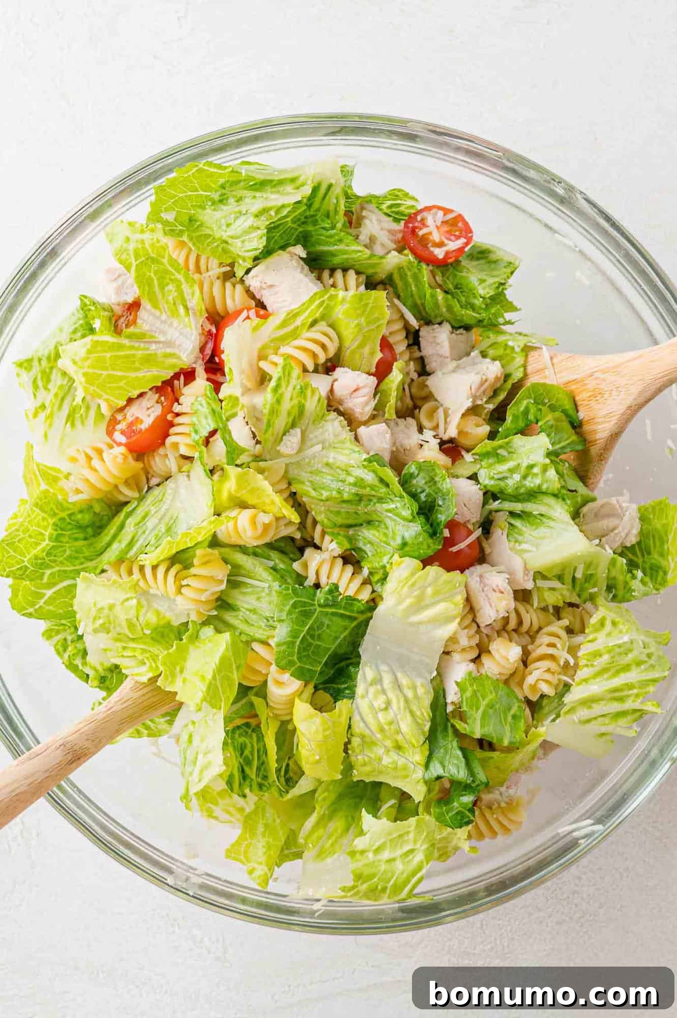 A large bowl of Chicken Caesar pasta salad ingredients being tossed vigorously, ensuring an even distribution of all components before the dressing is added.