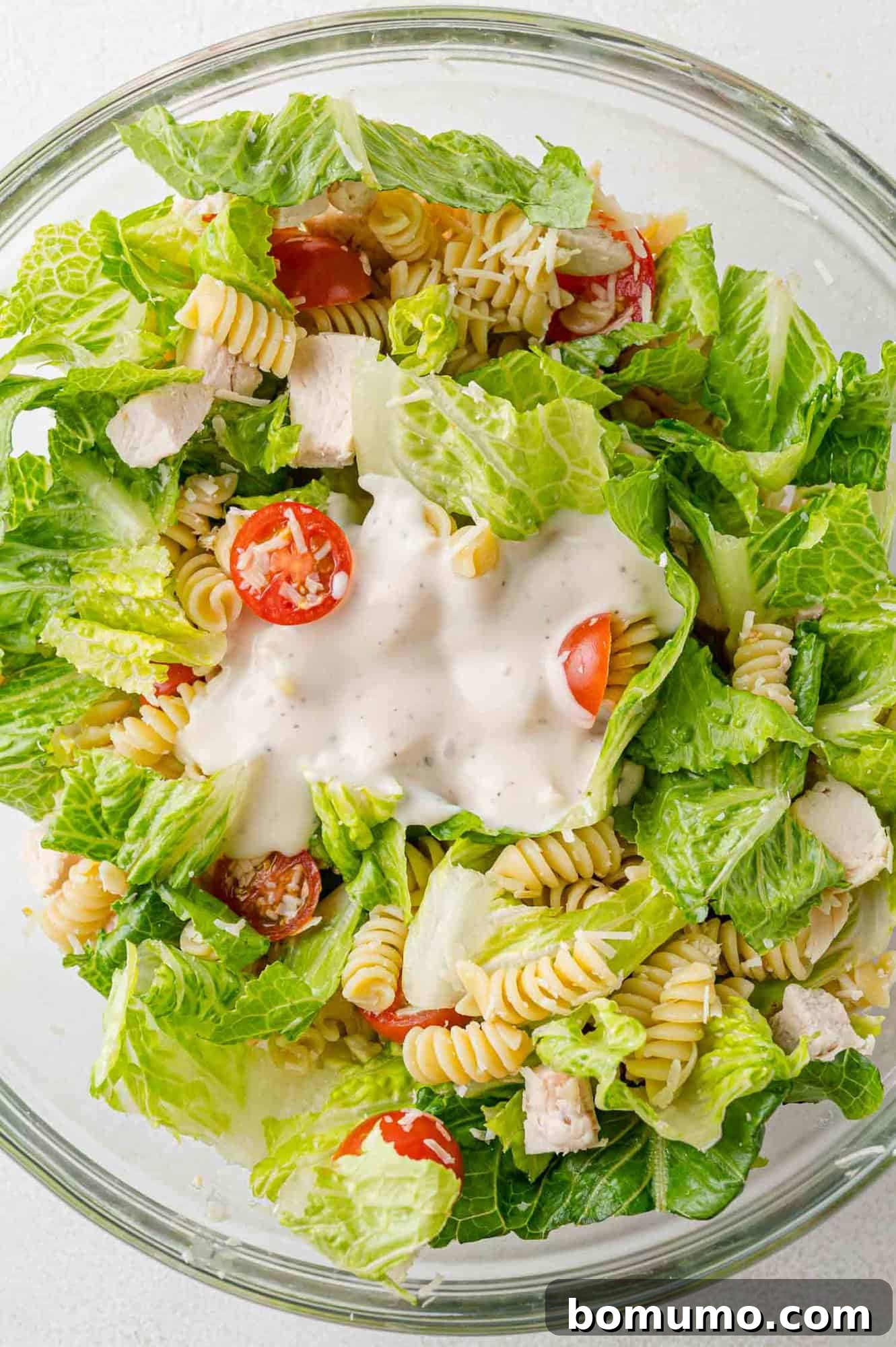 Creamy Caesar dressing artfully drizzled over the mixed Chicken Caesar pasta salad ingredients, waiting to be tossed and fully incorporated for maximum flavor.