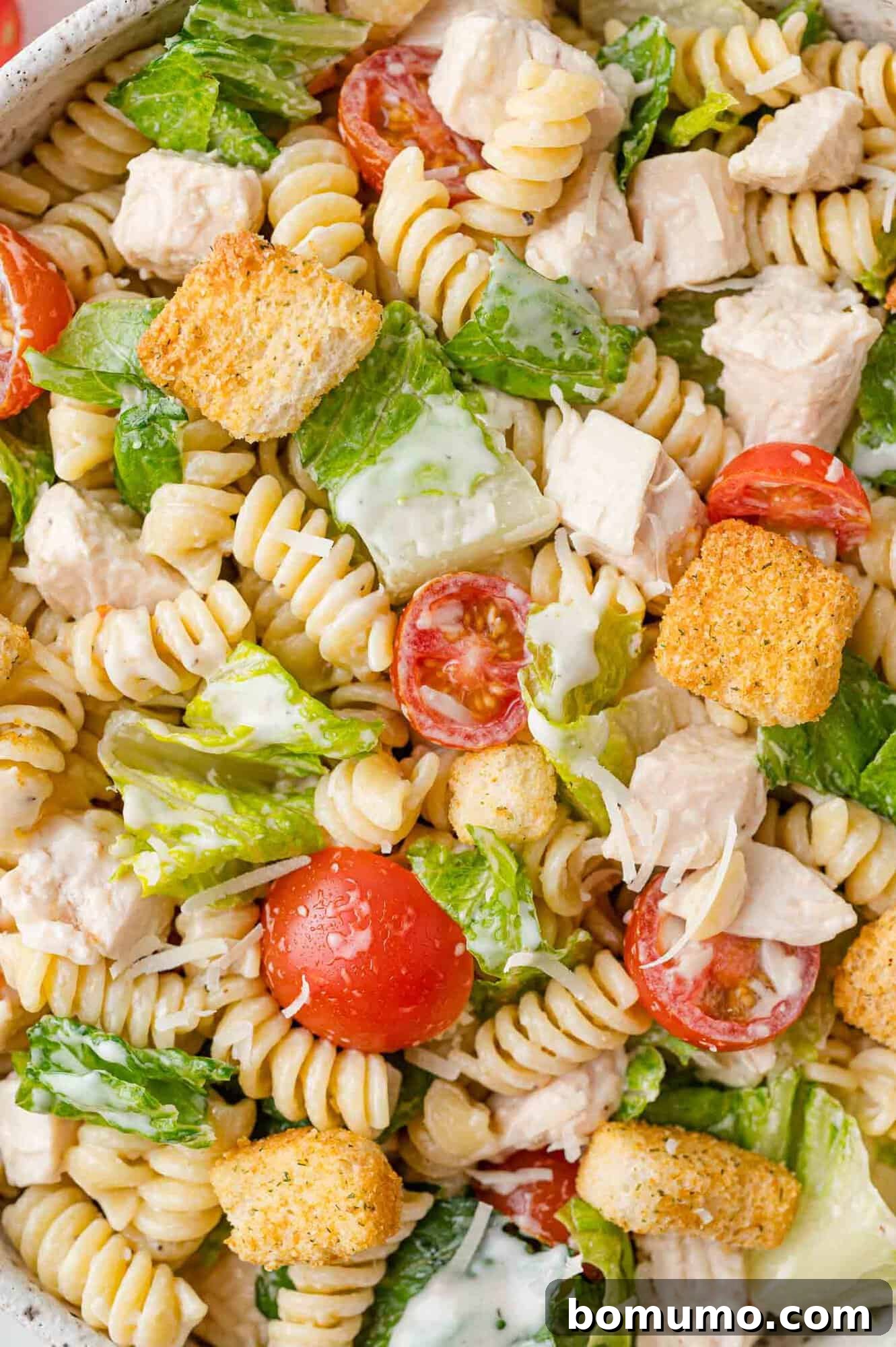 A close-up, mouth-watering view of the finished Chicken Caesar pasta salad, generously filling the frame, highlighting its rich textures and vibrant colors.
