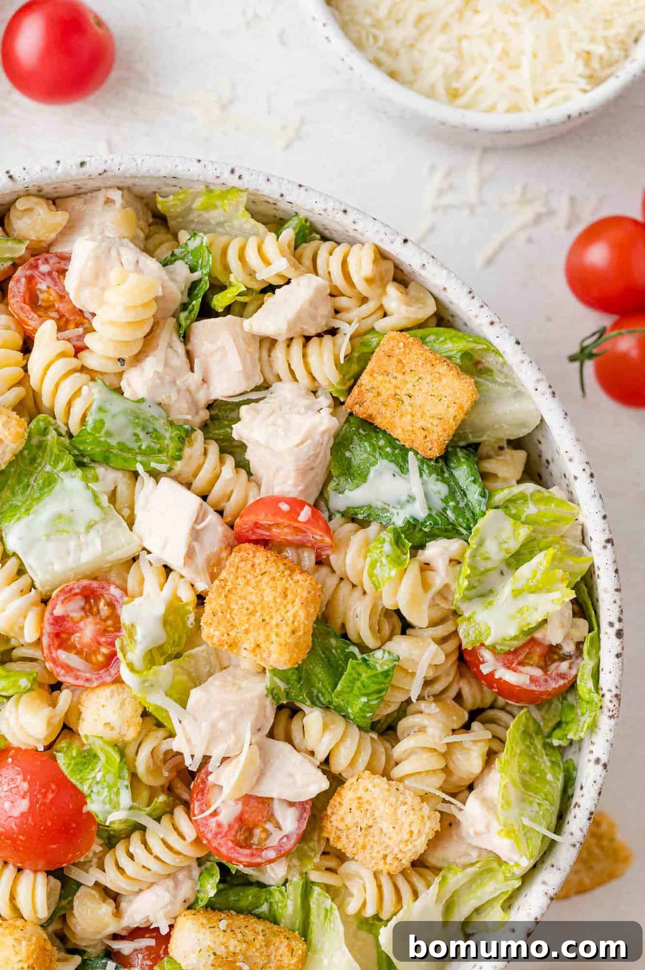 A beautifully composed shot of Chicken Caesar pasta salad, featuring distinct cherry tomatoes and generous sprinkles of Parmesan cheese, highlighting its appealing textures and colors.
