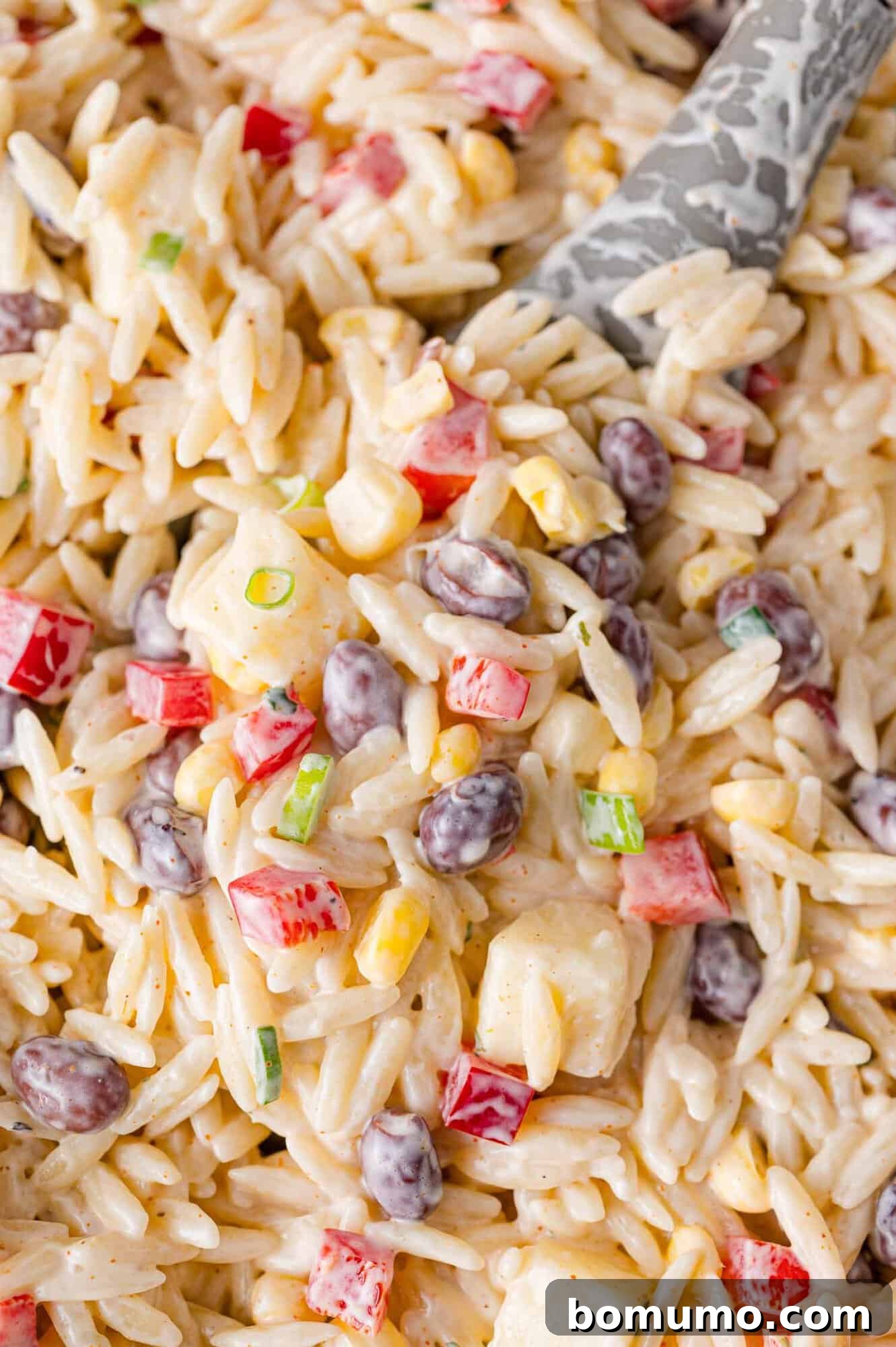 Creamy southwestern orzo salad on a serving spoon and in a large bowl, showcasing its vibrant colors and inviting texture.