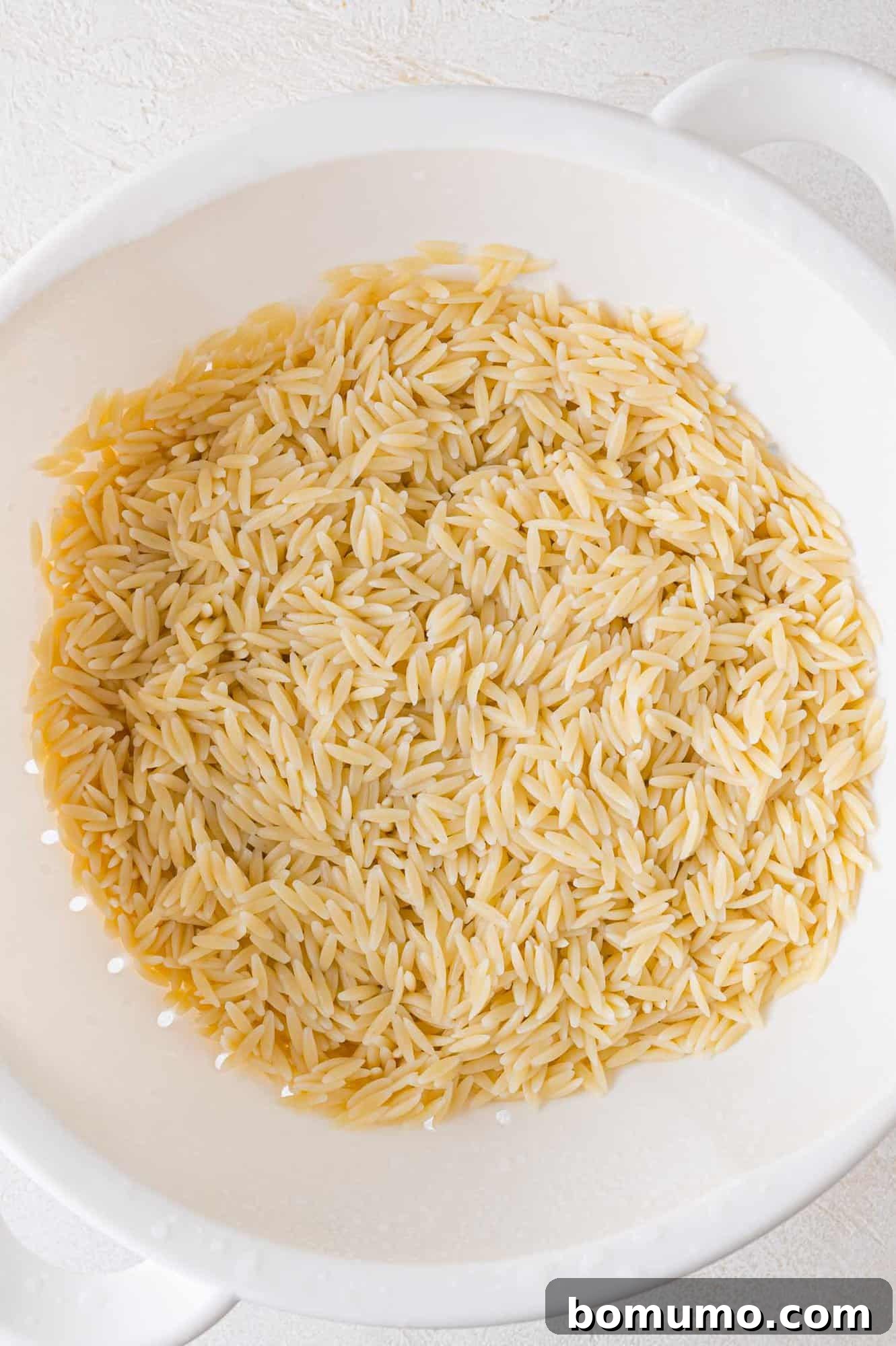 Freshly cooked orzo pasta cooling in a colander under cold running water, ready for salad preparation.