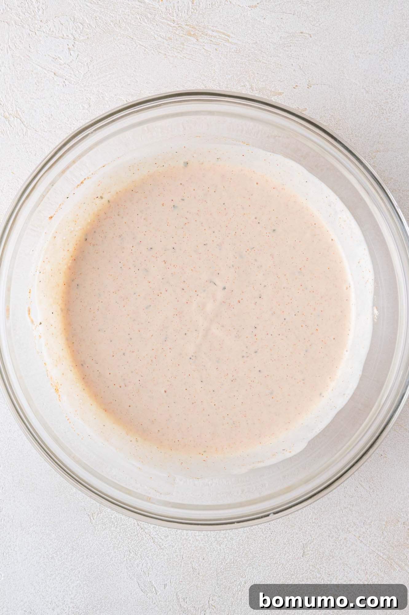 The smoothly whisked ranch-taco dressing, glistening in a clear glass bowl, ready to be added to the salad.