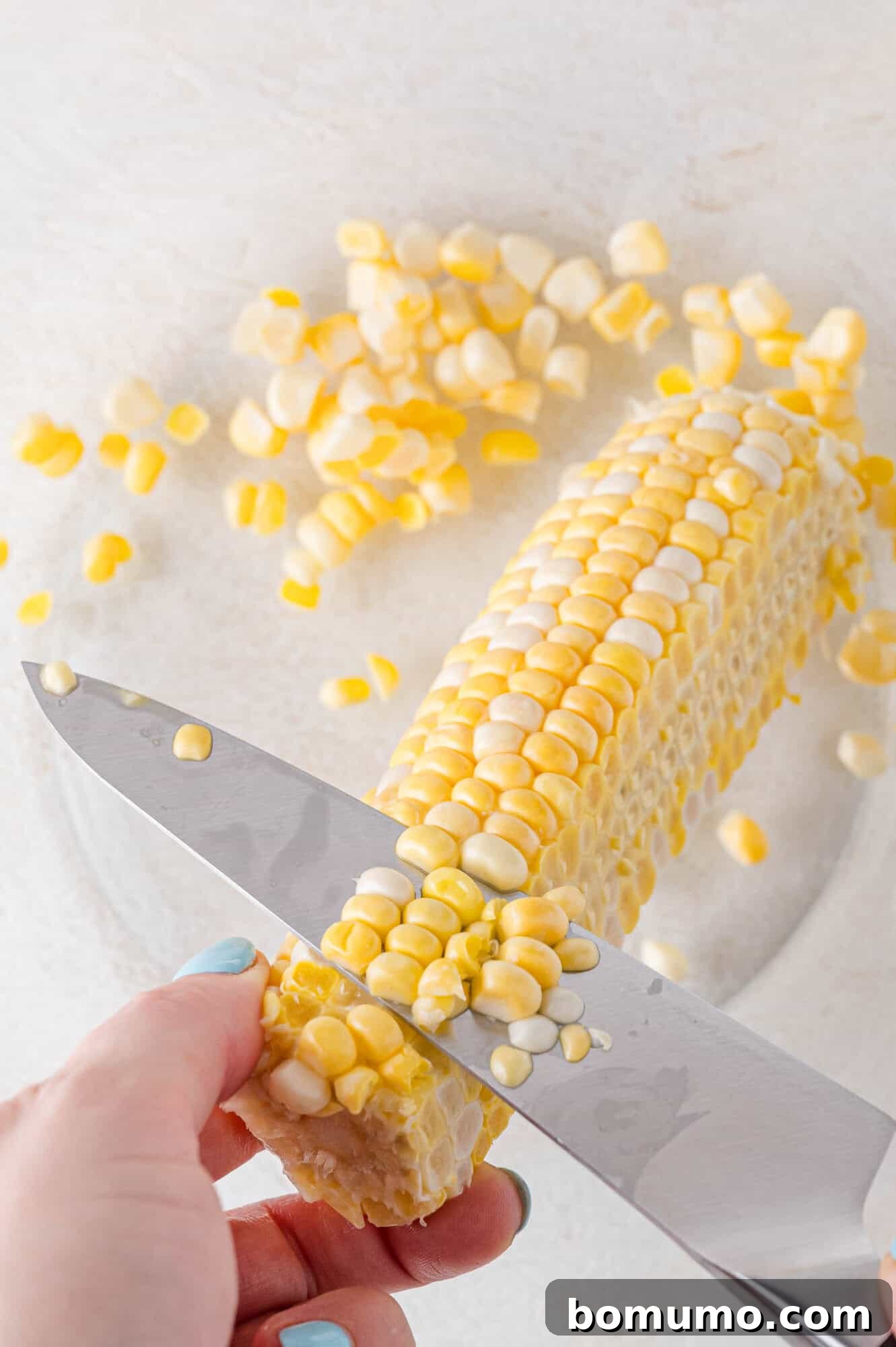 Fresh corn kernels being expertly sliced off the cob and collected in a large bowl, demonstrating a clean preparation technique.