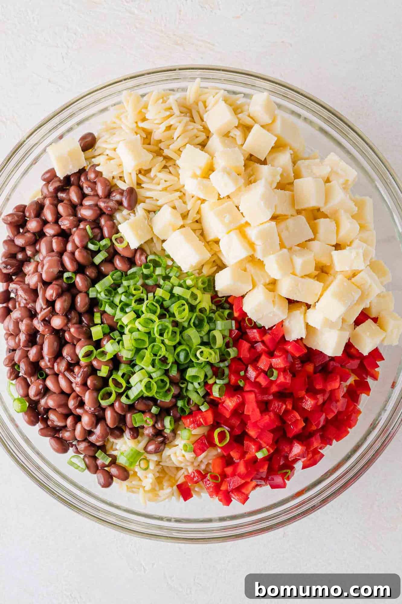 A large mixing bowl filled with all the vibrant ingredients of the orzo salad, excluding the dressing, ready for the final step.