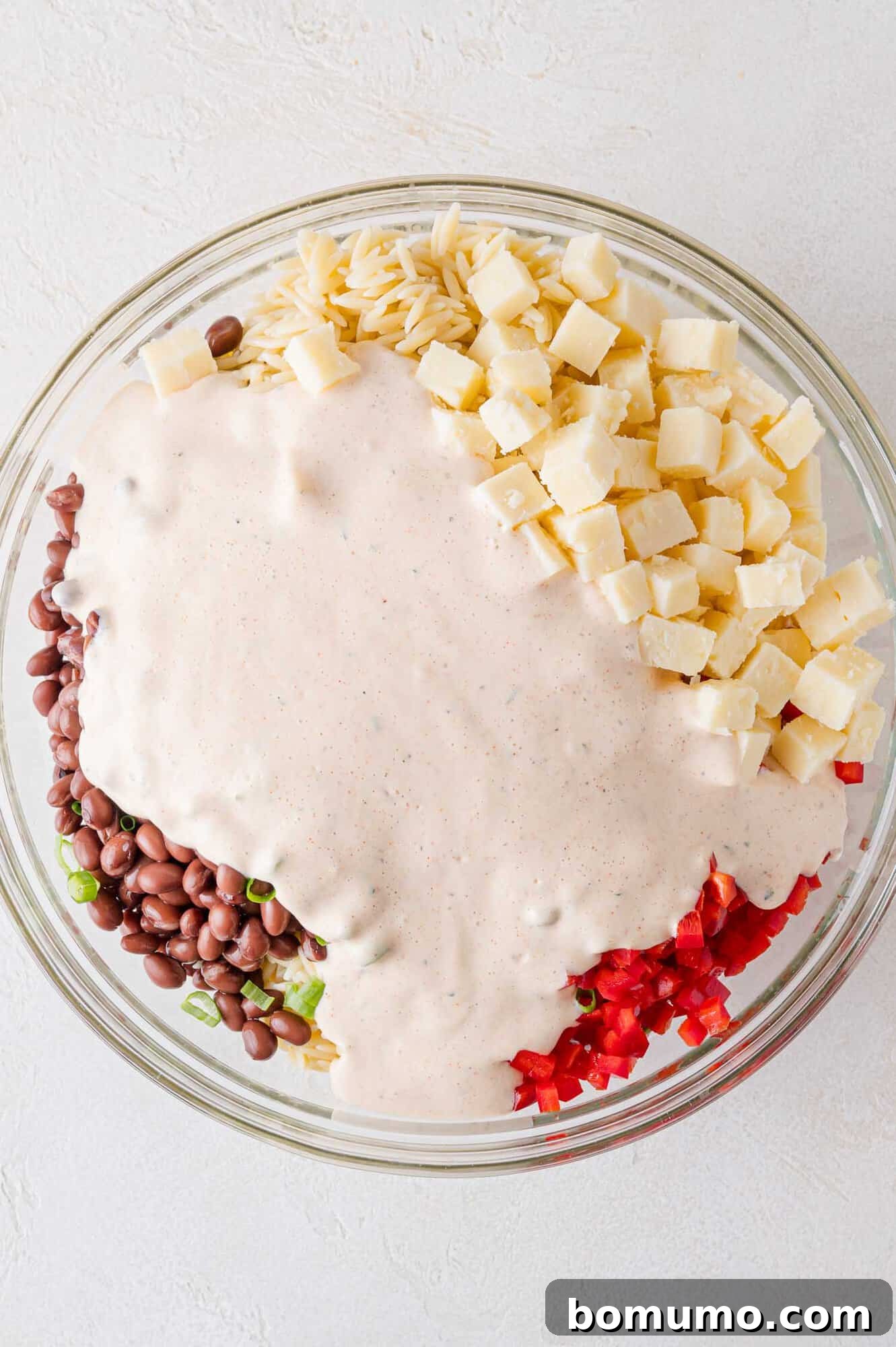 The creamy southwestern dressing being poured generously over the colorful salad ingredients in a large mixing bowl.