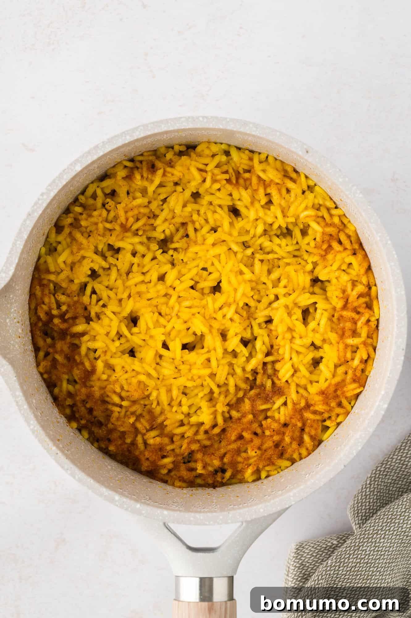 A pot of freshly cooked yellow rice resting on a light countertop, with a decorative fabric napkin nearby.