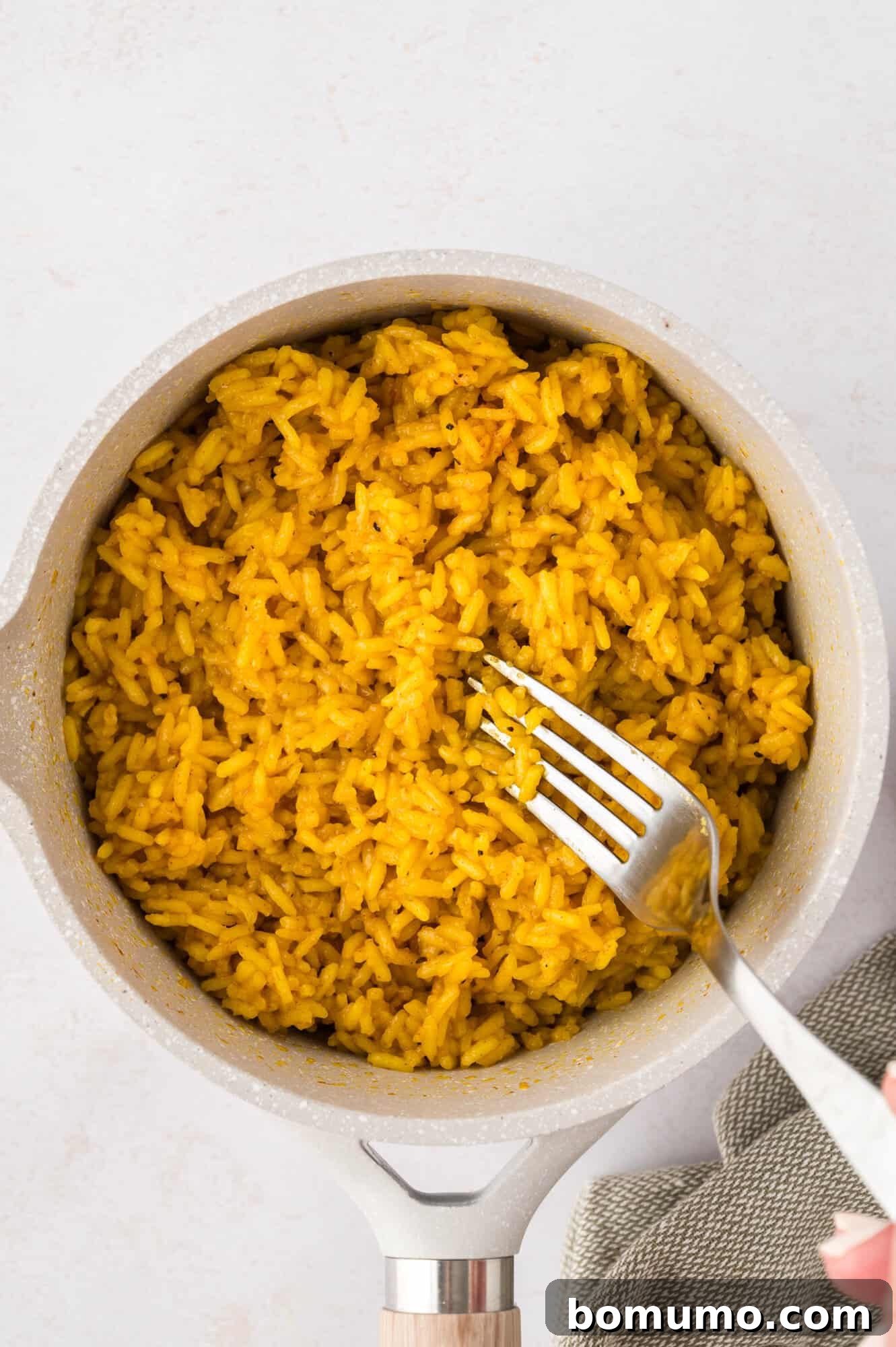 A pot of fluffy yellow rice on a light surface, with a fork gently fluffed into the grains, ready for serving.
