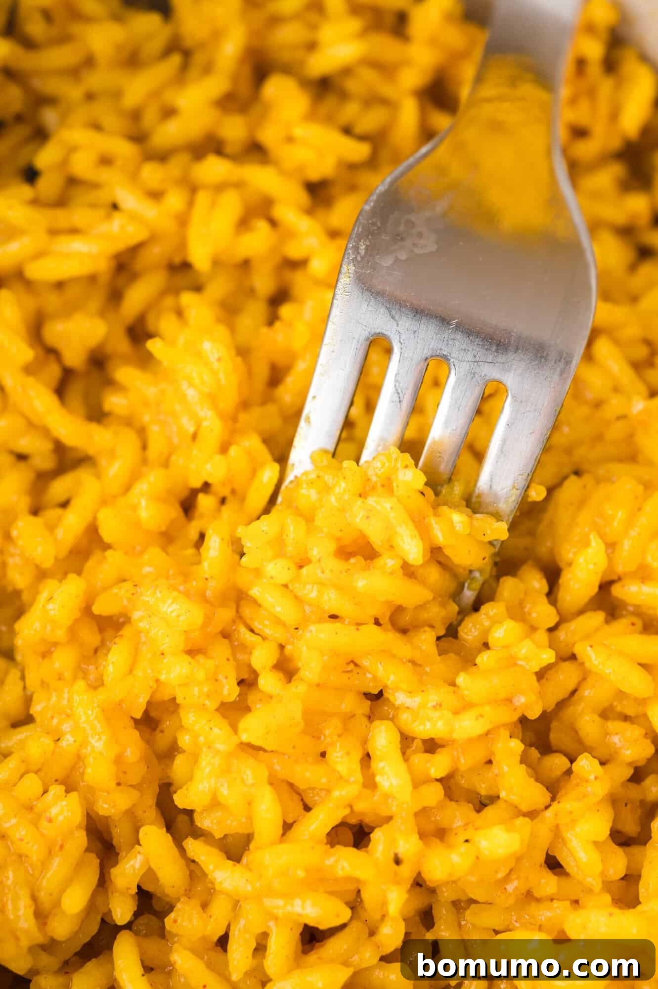 A close-up shot of a fork lifting a portion of fluffy yellow rice, showcasing its perfect texture and vibrant color.