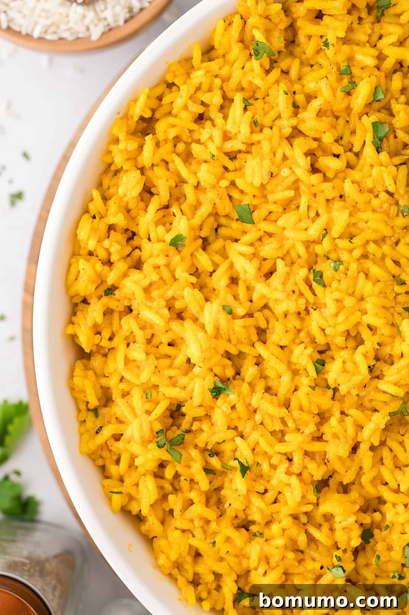 A large white serving bowl generously filled with cooked yellow rice, beautifully garnished with small green herbs, ready to be enjoyed.