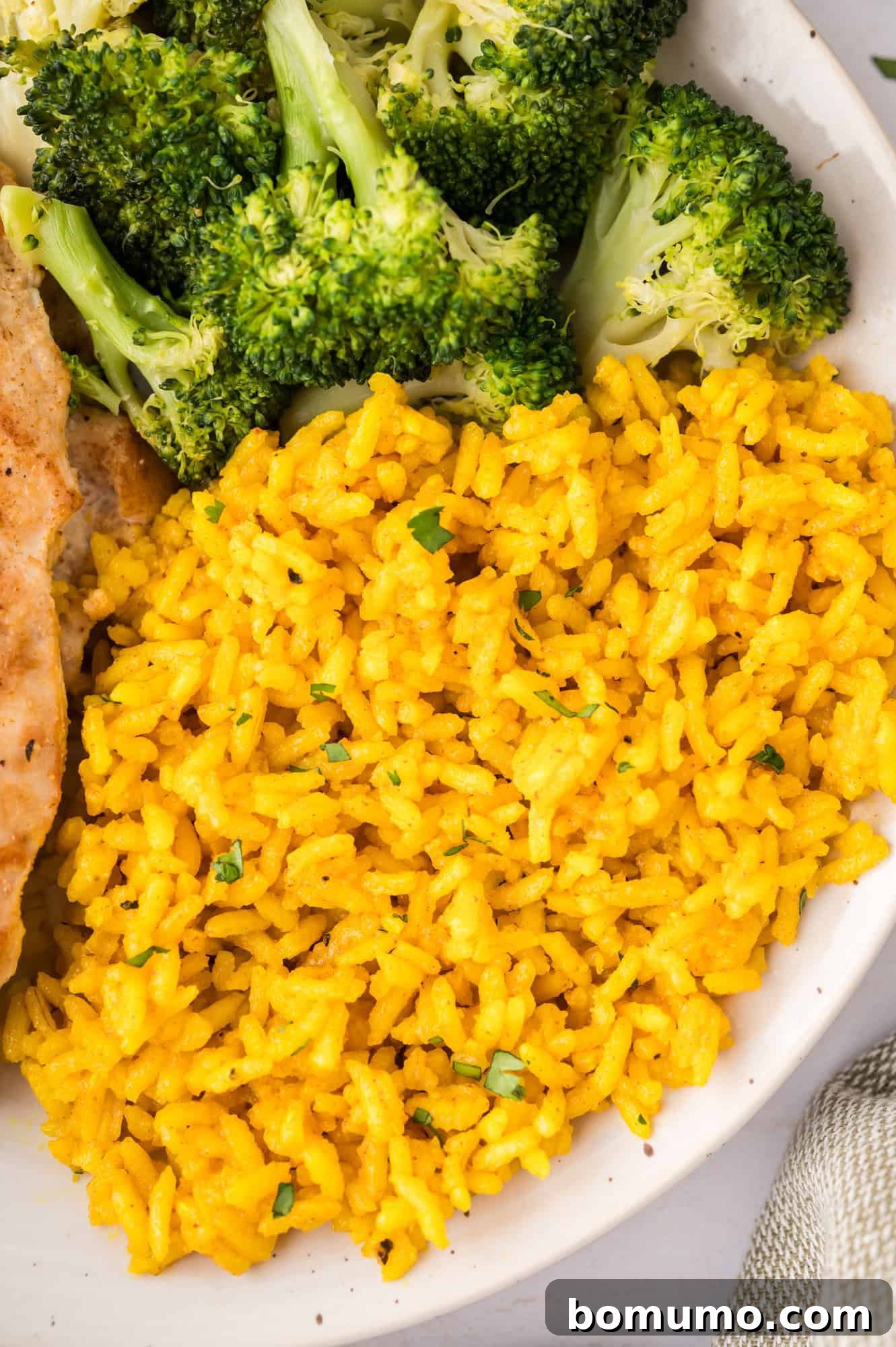 A beautifully plated dish featuring vibrant yellow rice, alongside a serving of fresh steamed broccoli and a perfectly grilled chicken breast, showcasing a complete and balanced meal.
