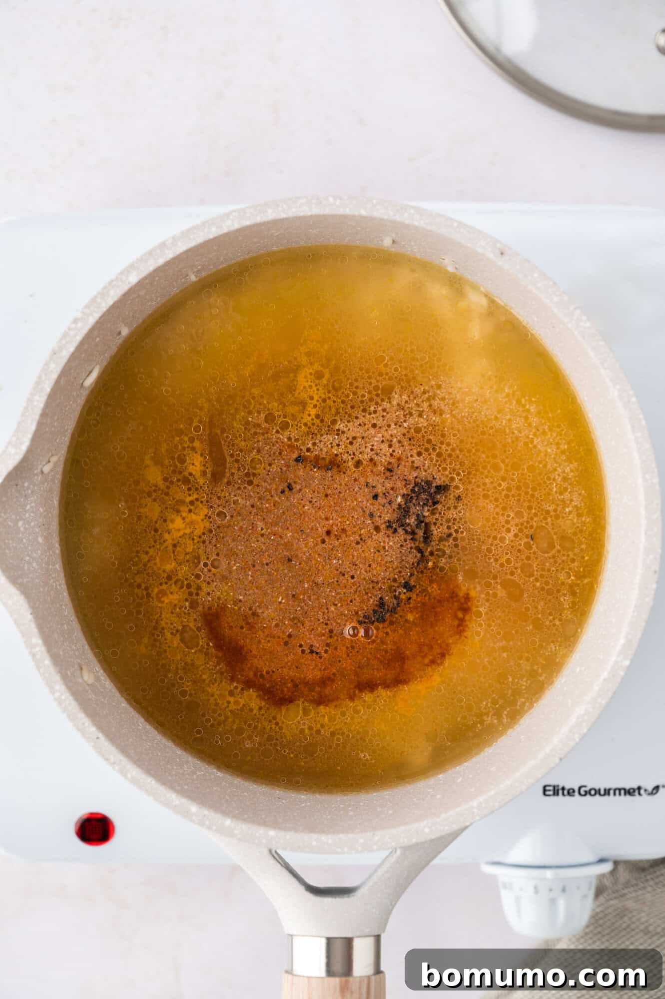 A pot on a stovetop with broth and spices simmering, showing small bubbles and the vibrant yellow color developing.