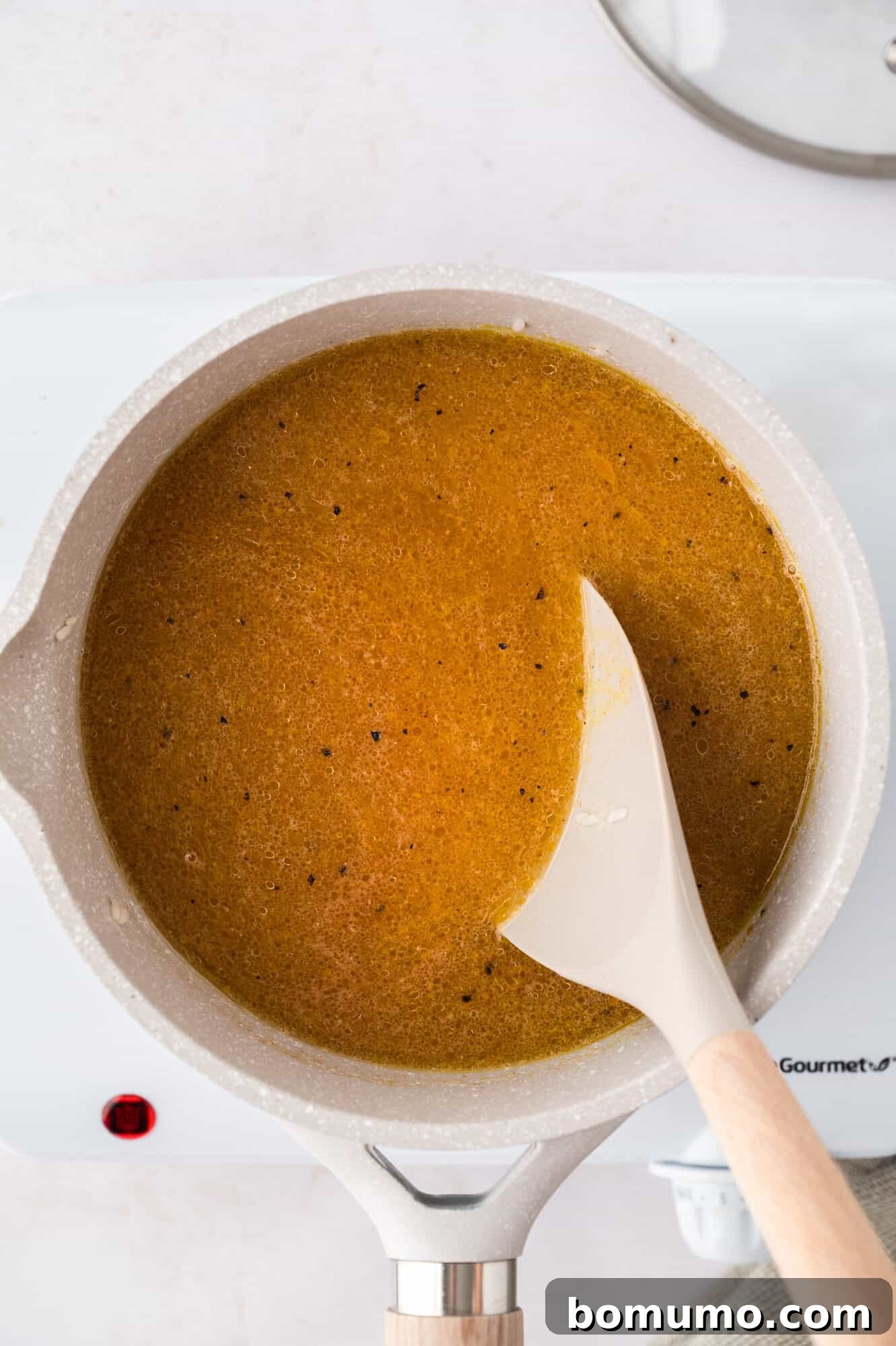 A white spatula stirring the yellow rice mixture in a saucepan on a stovetop, ensuring spices are well combined.