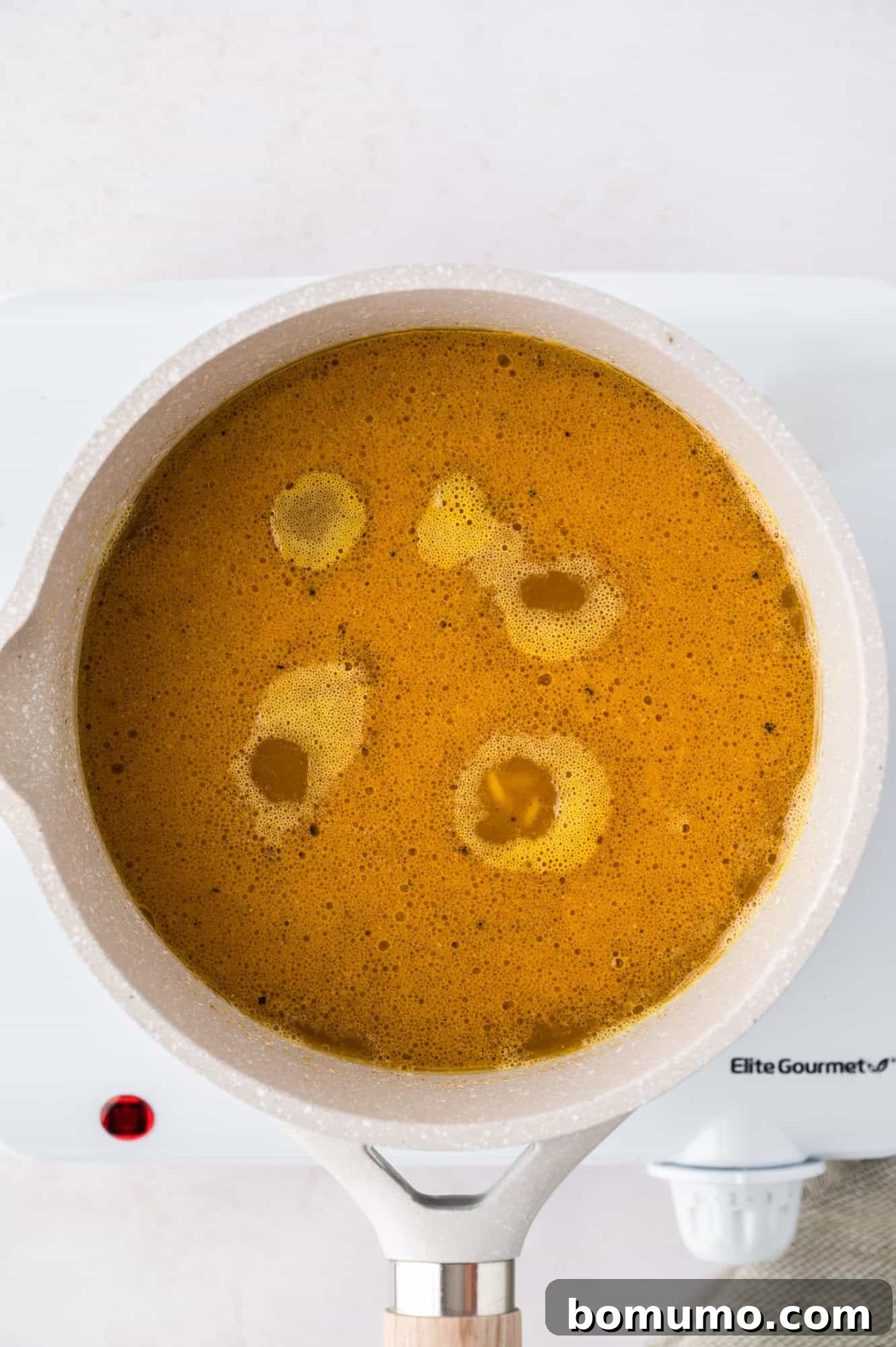 A saucepan filled with the yellow rice mixture, simmering gently on a white stovetop burner, showing the liquids reducing.