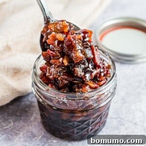A small jar of homemade bacon jam being scooped out with a spoon, highlighting its rich, chunky texture and glossy finish.