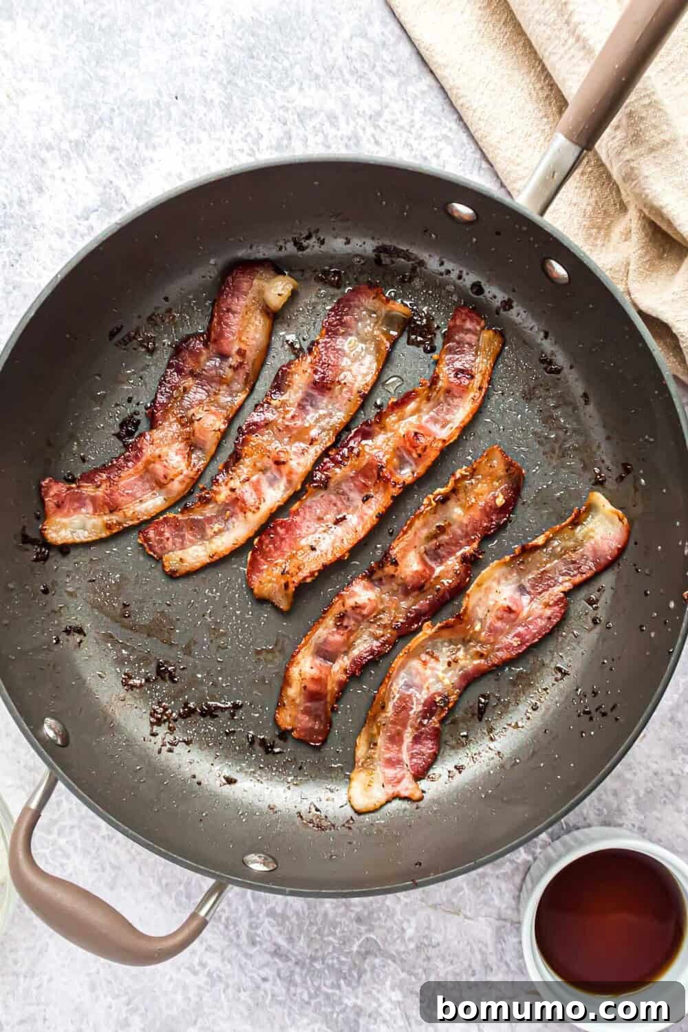 Sweet & Savory Bacon Jam 4 Strips of bacon sizzling and cooking in a large cast-iron frying pan, rendering fat and browning to a perfect crisp.