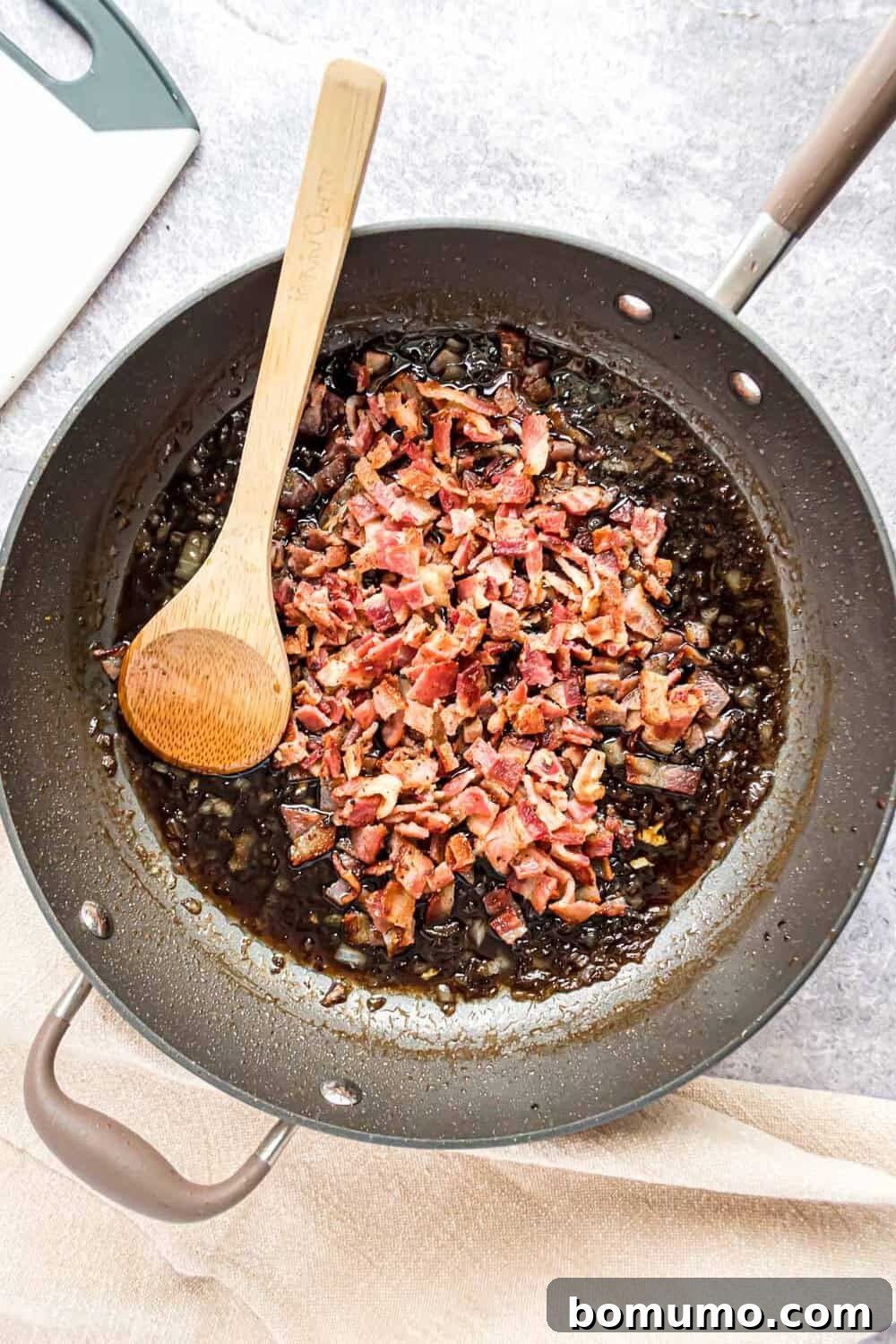 Sweet & Savory Bacon Jam 9 Chopped crispy bacon pieces being stirred back into the simmering, thickened jam base in the frying pan, combining all the delicious elements.