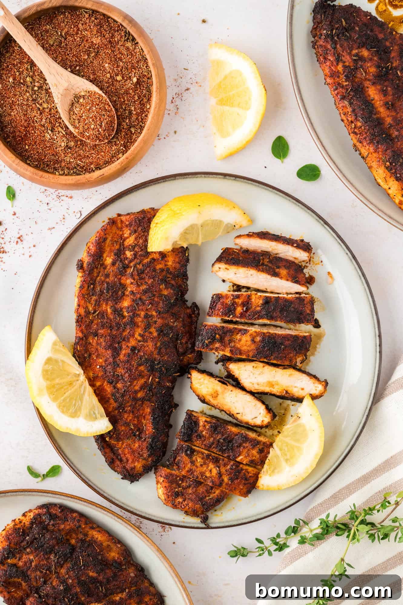 Blackened chicken on a plate, partially sliced, with lemon slices.