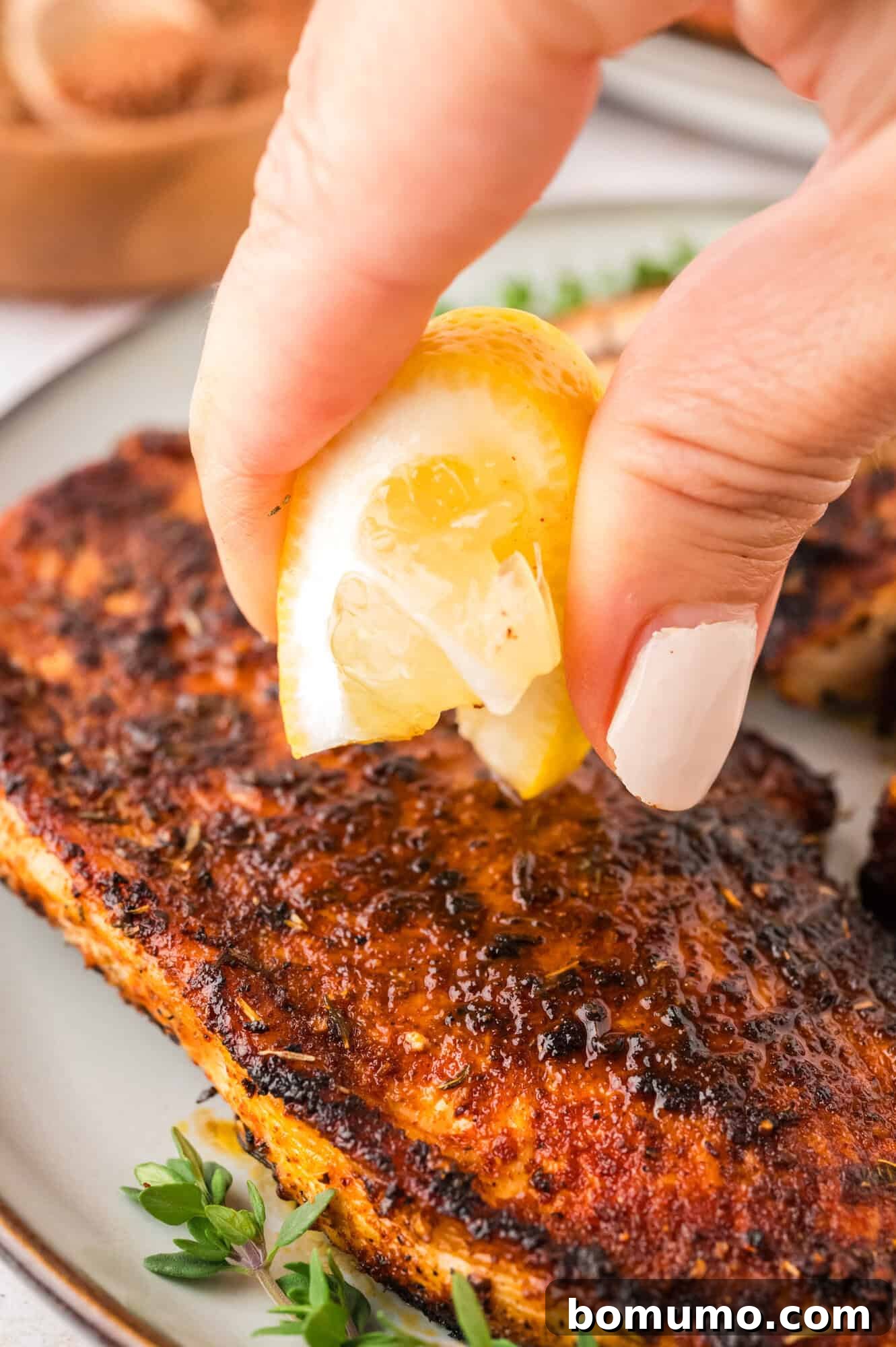 Lemon being squeezed onto blackened chicken.