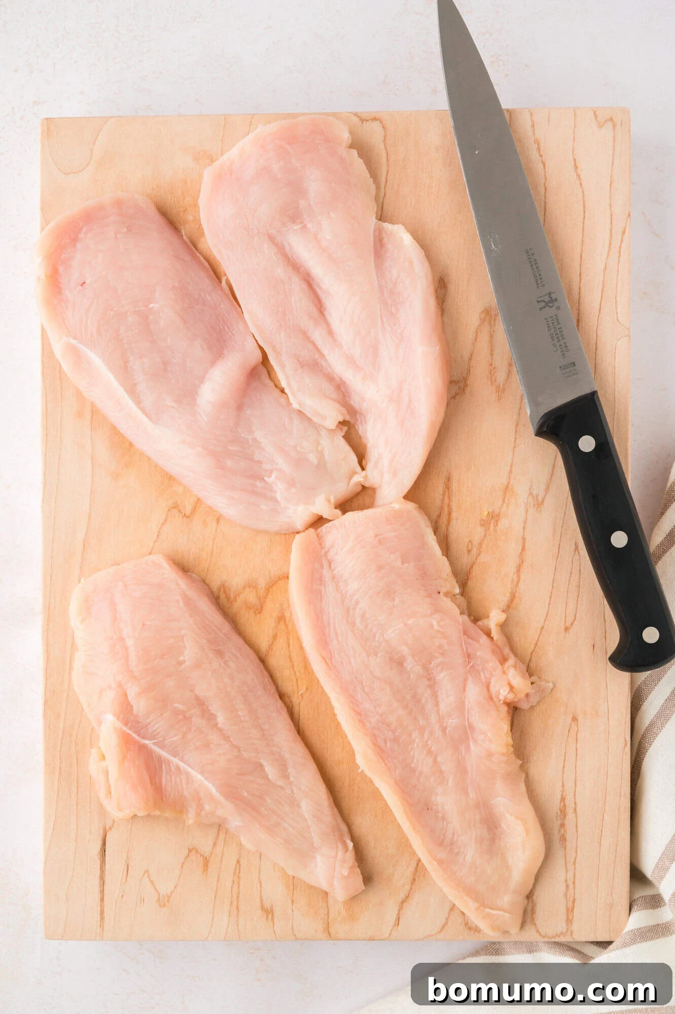 Multiple chicken cutlets and a knife on a cutting board.