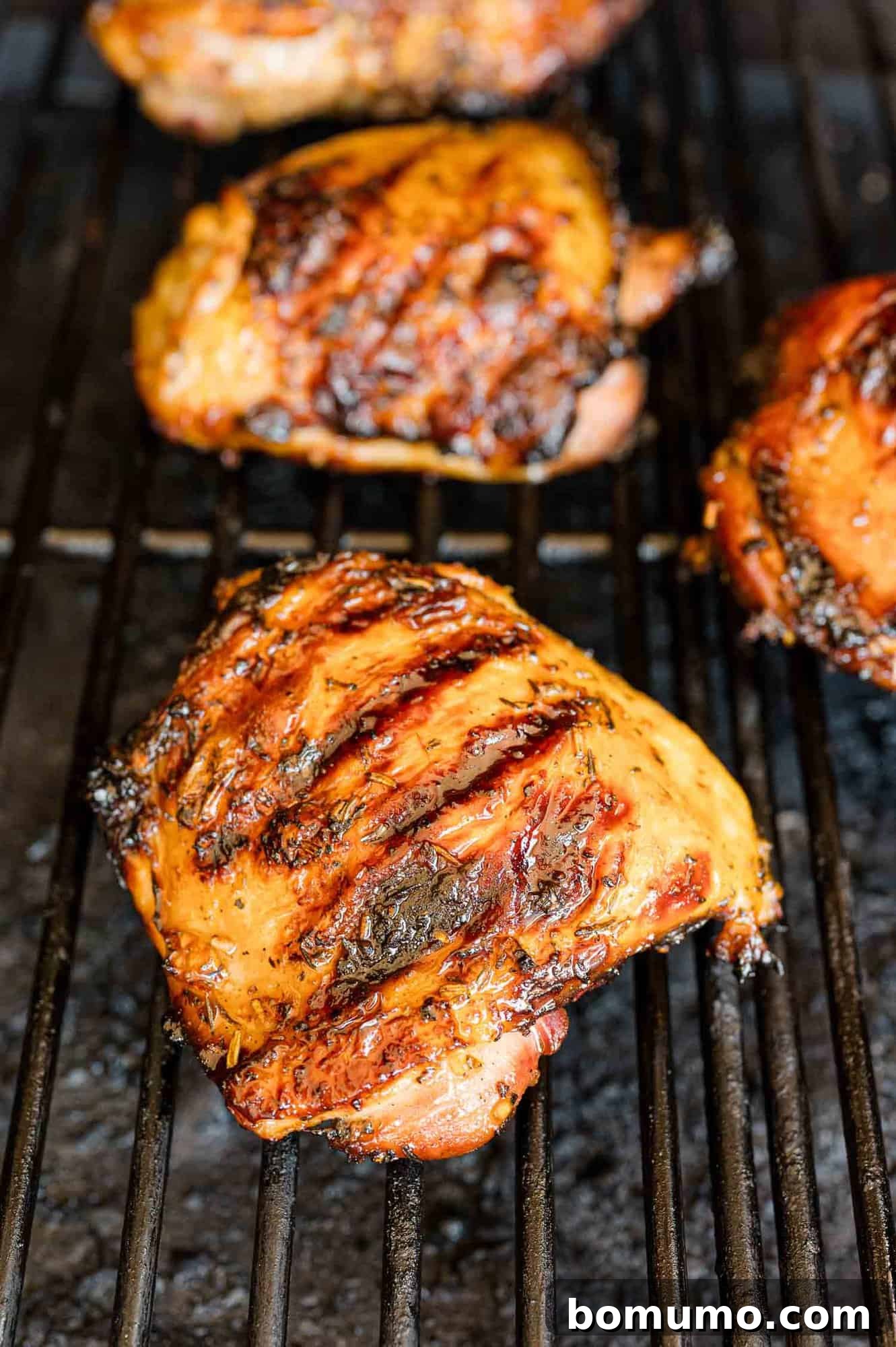 Perfectly grilled chicken thighs, still sizzling on the grill grates, showing off their golden-brown char.