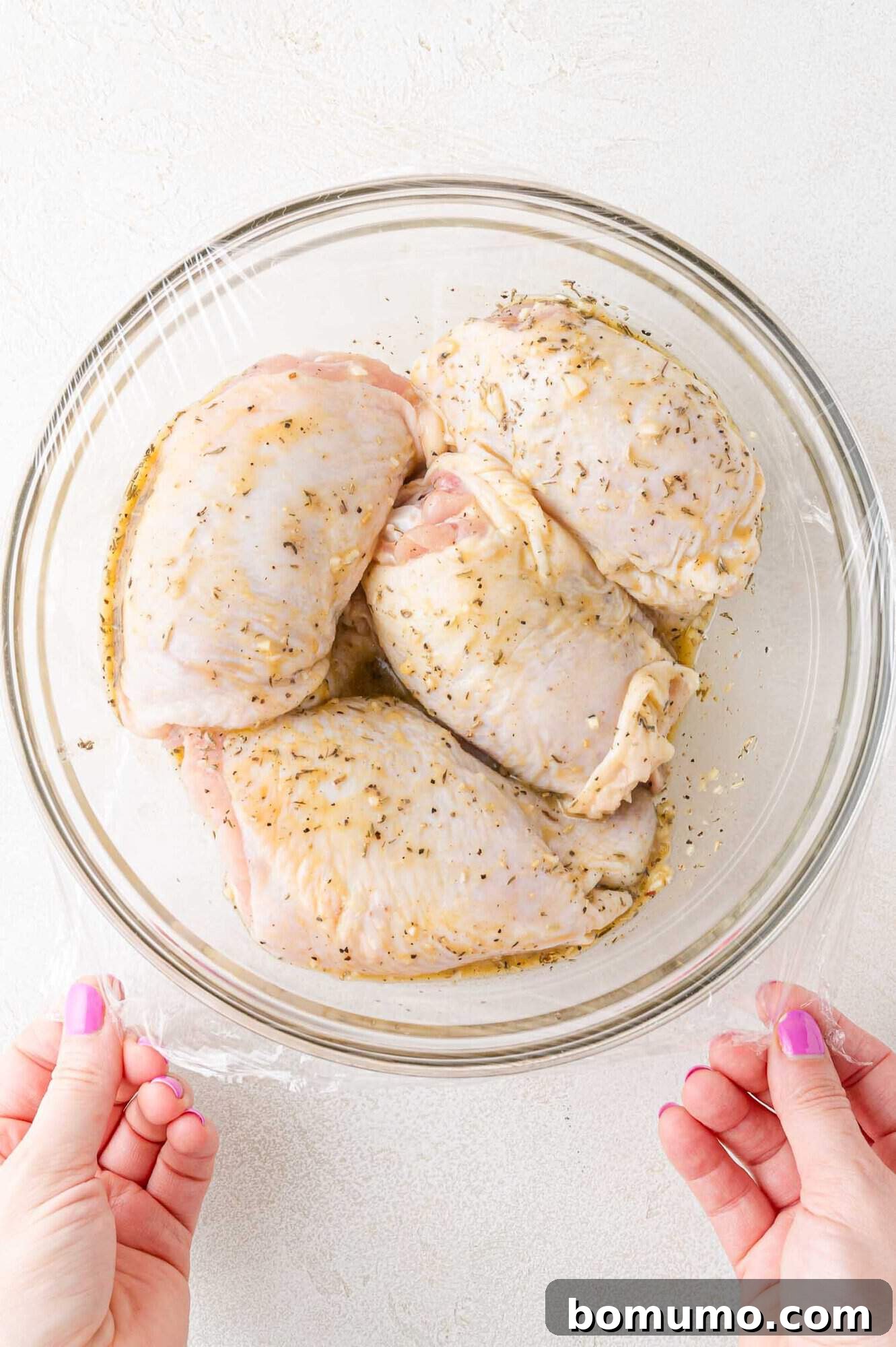 Chicken thighs soaking in the aromatic marinade within a clear glass bowl, absorbing all the delicious flavors.
