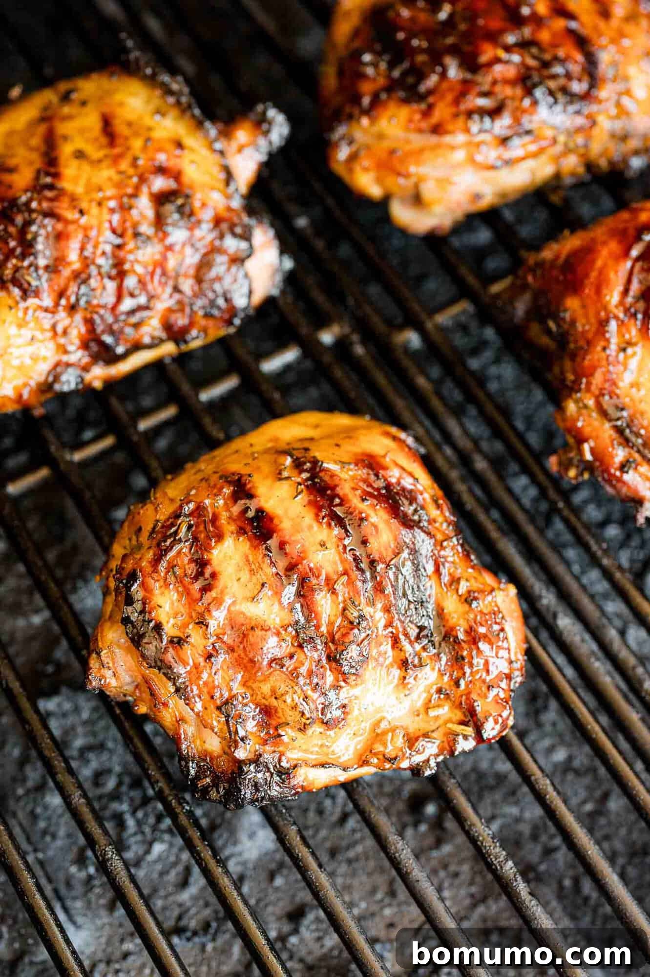 Chicken thighs sizzling and charring on a hot grill, flames occasionally licking the edges.