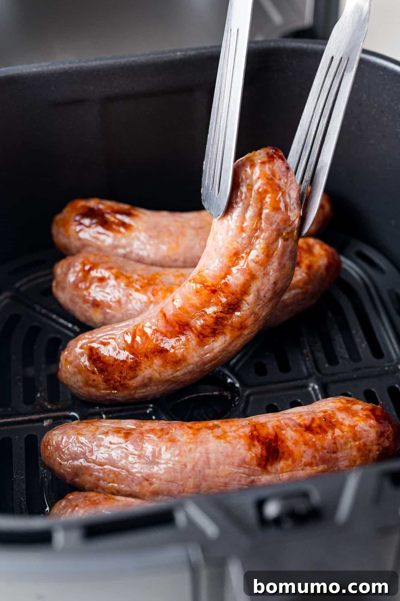 Air fryer brat being lifted out of an air fryer with tongs.